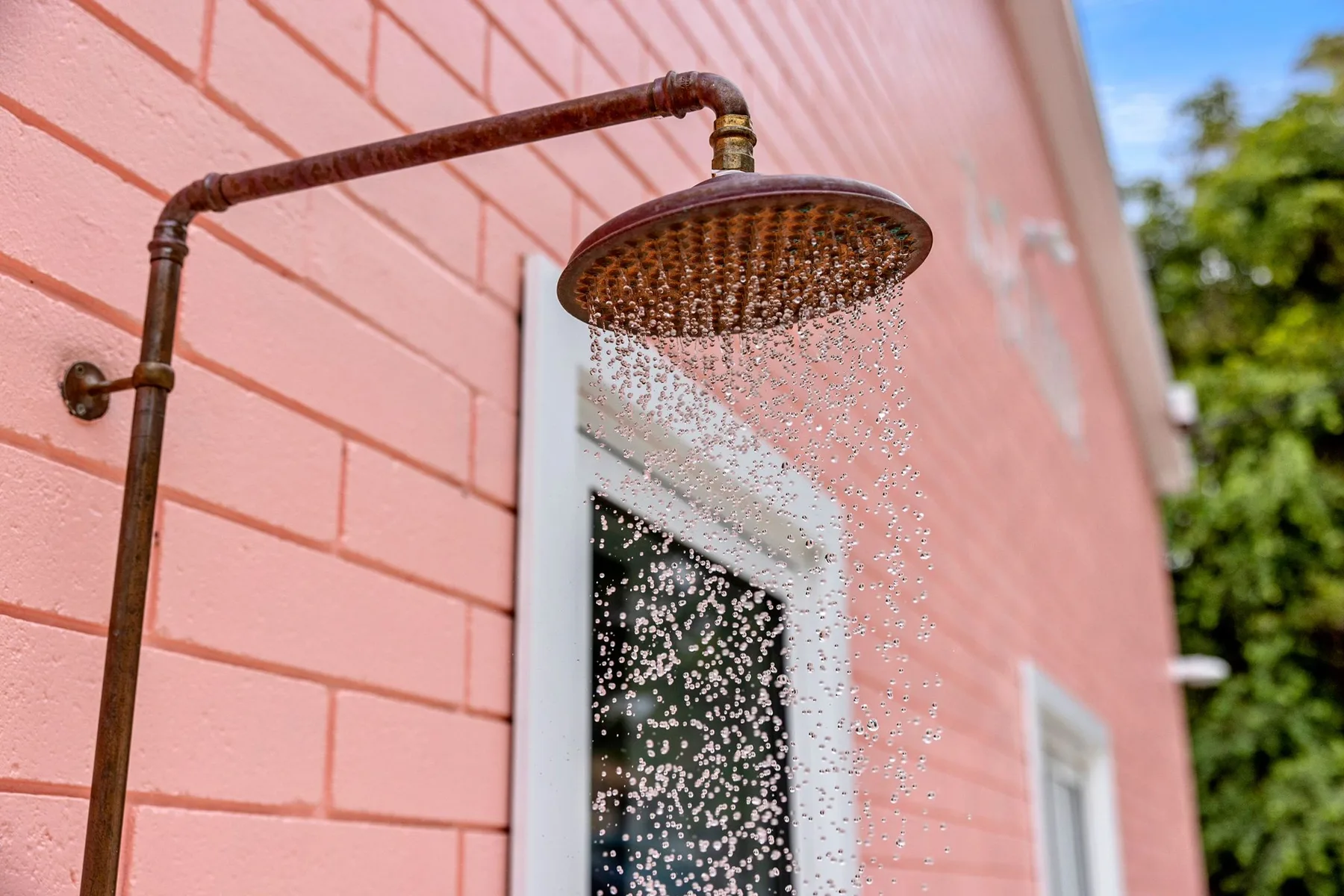 Una ducha exterior rocía agua junto a una pared exterior rosa.