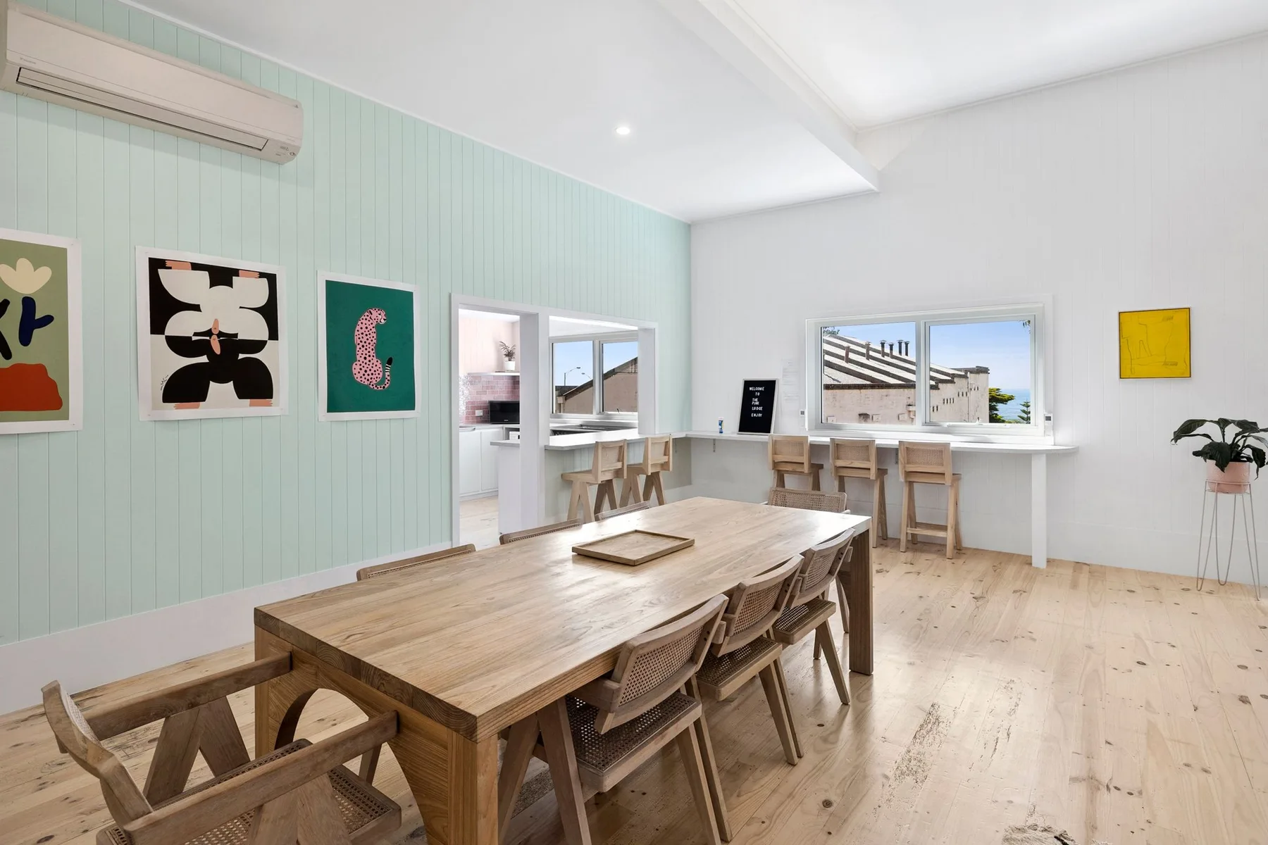 Un comedor luminoso con una mesa larga de madera y cuadros en las paredes.
