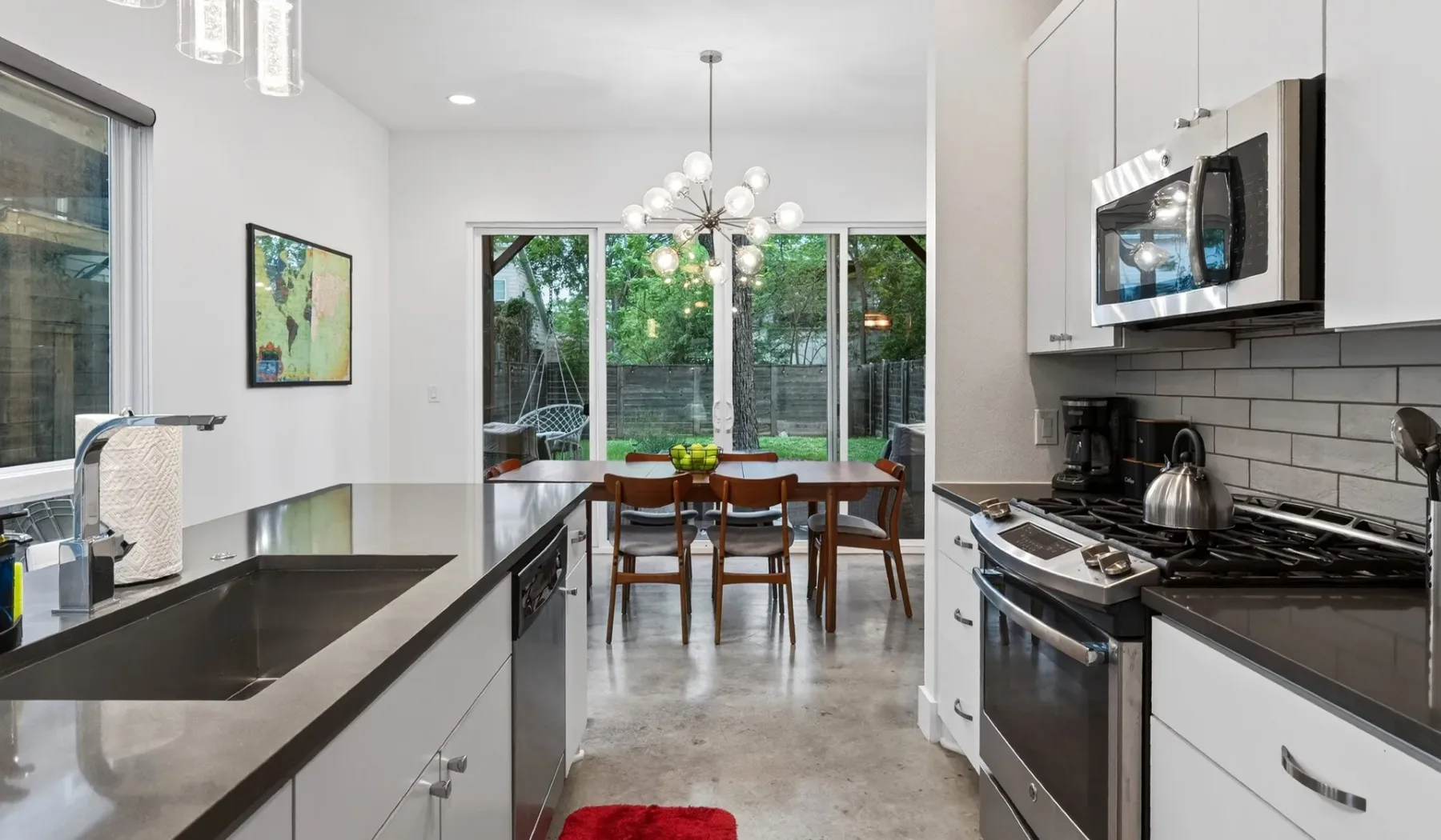 A modern kitchen opens onto a dining area with a table beside large windows.