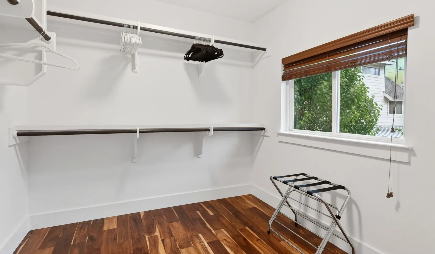 A bright walk-in closet with hanging rails and a window overlooking greenery.