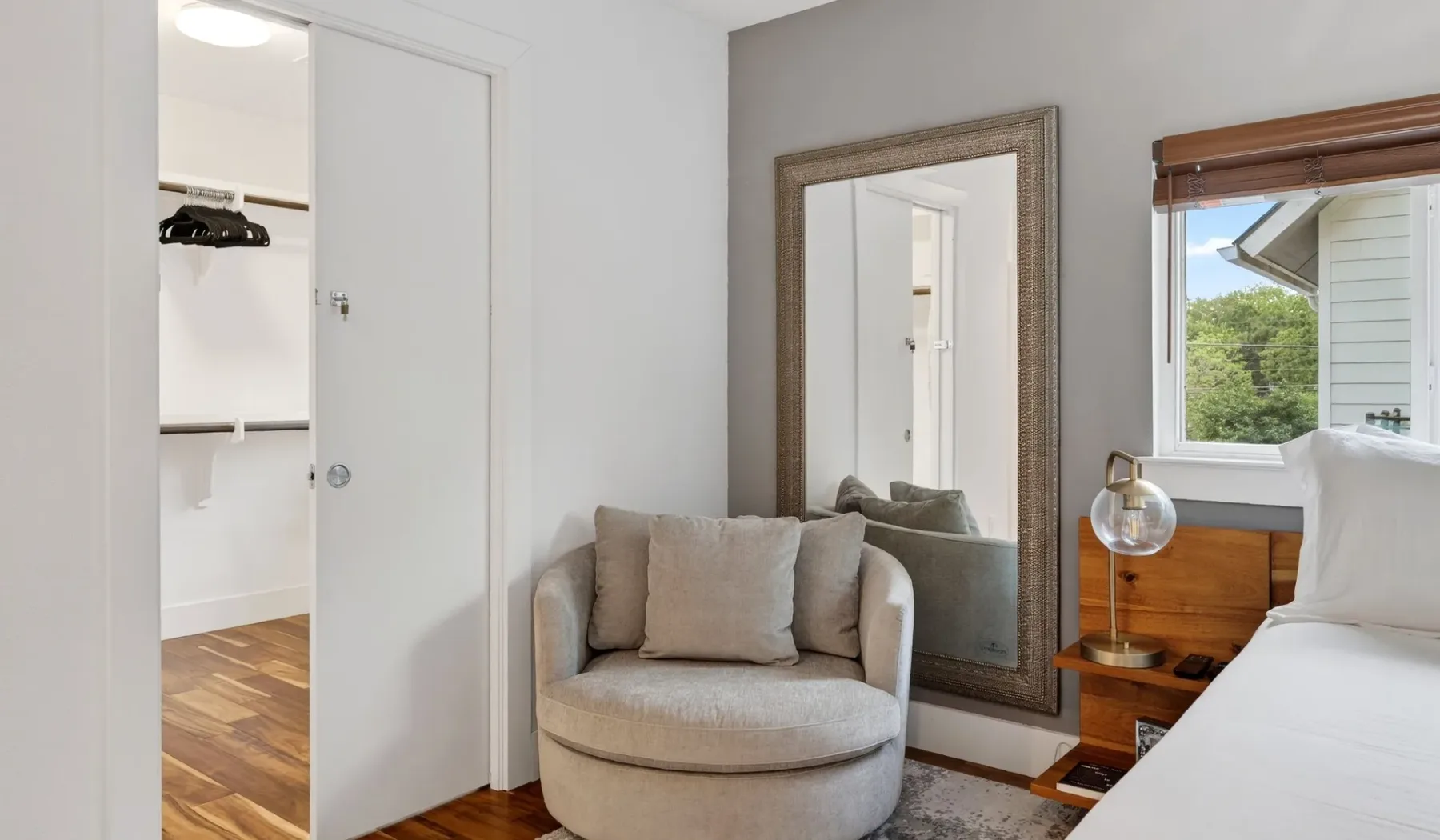 A bedroom seating area with a cushioned chair beside a large mirror.