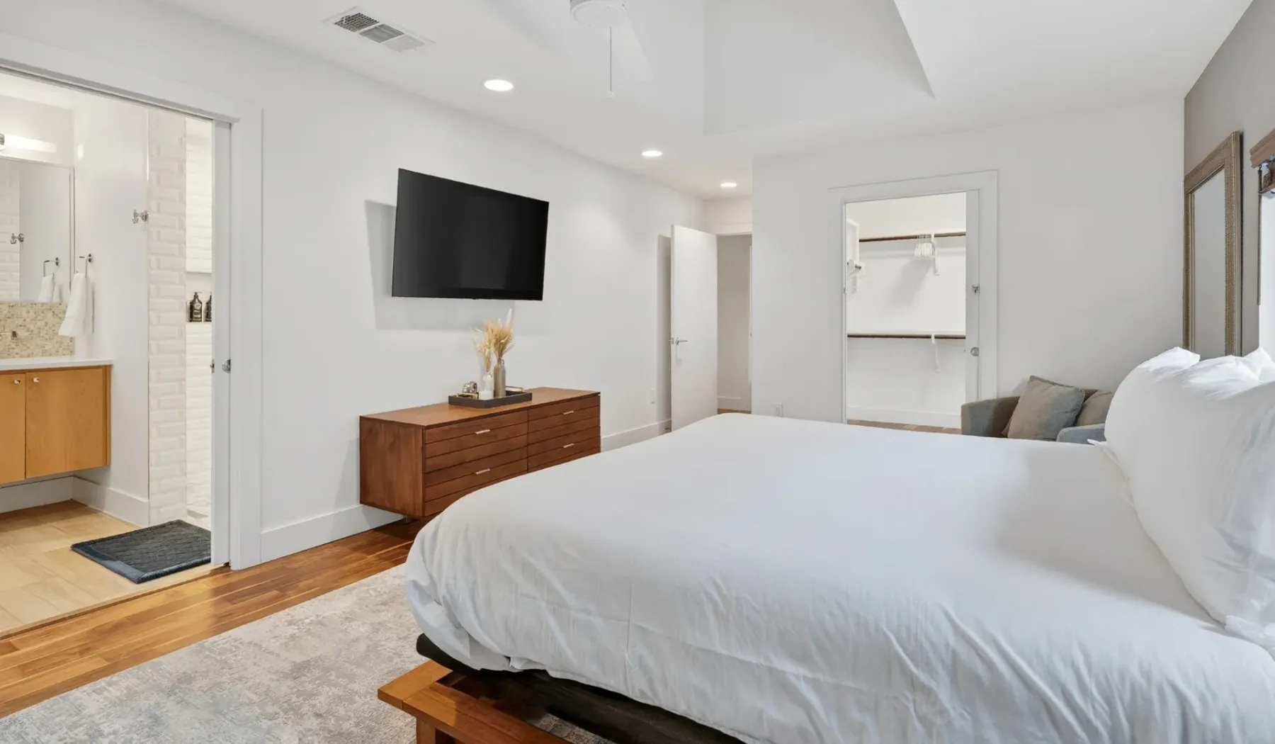 A bright bedroom with a large bed, wall-mounted television, and adjoining bathroom.