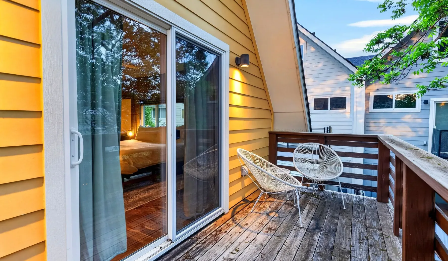 A wooden deck with two chairs sits beside a sliding glass door.