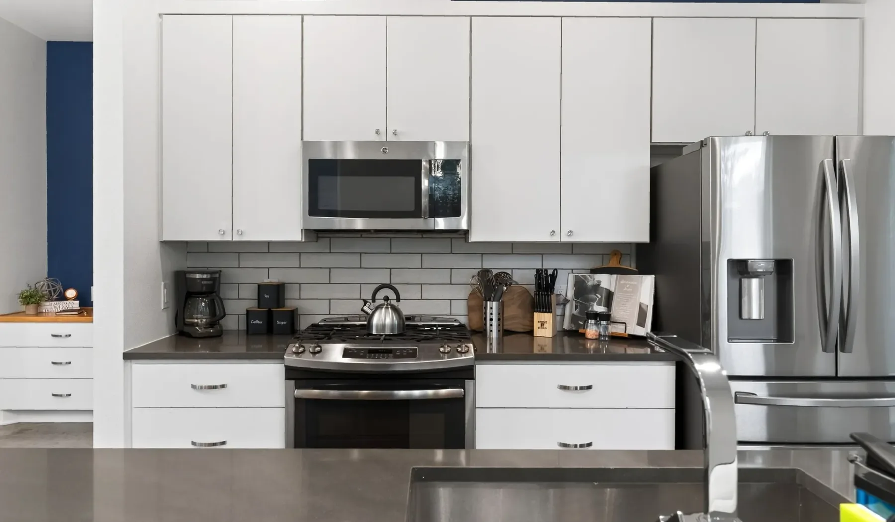A modern kitchen with white cabinets, stainless steel appliances, and a dark countertop.