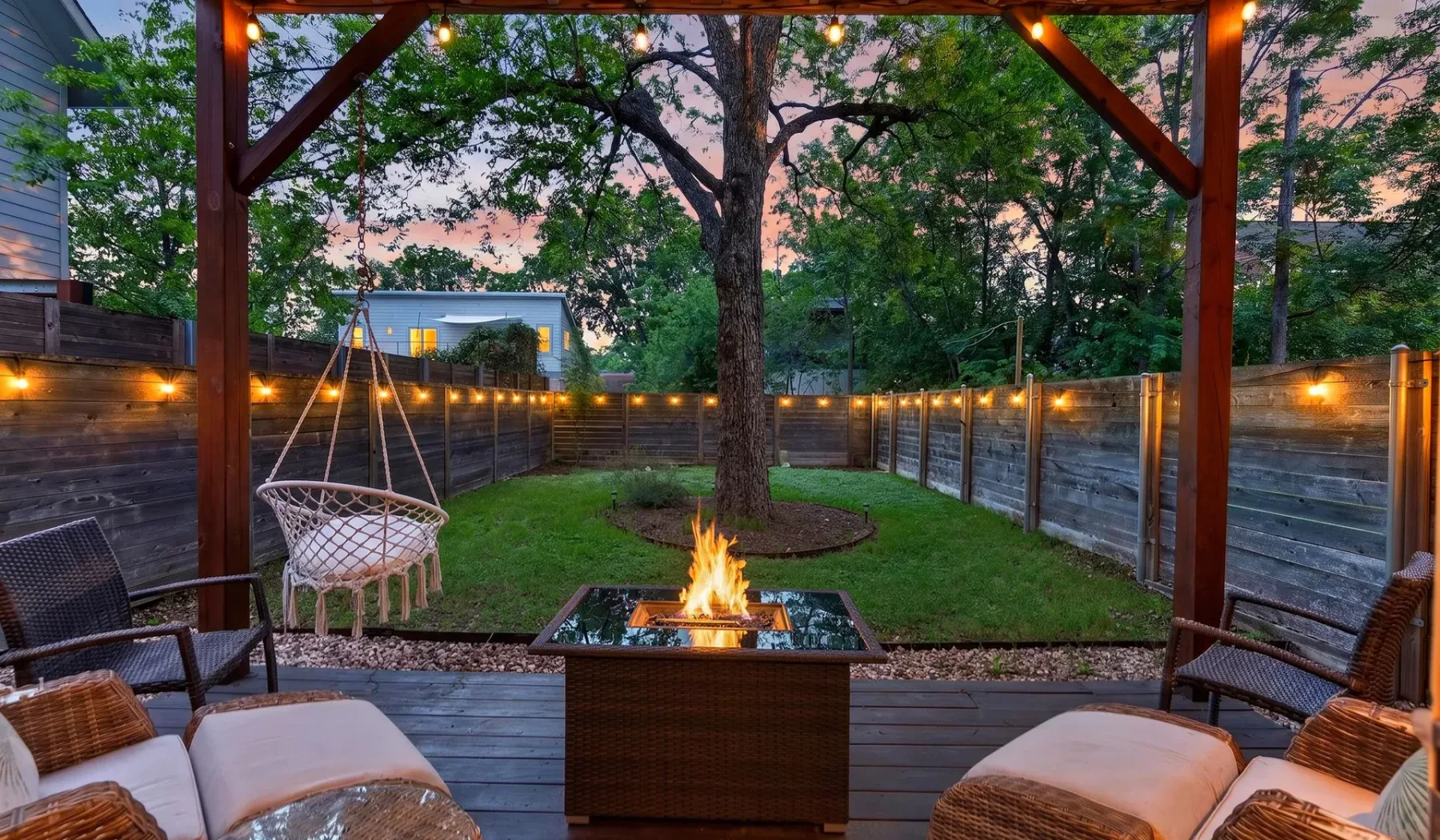An outdoor seating area surrounds a fire pit beneath a wooden pergola.
