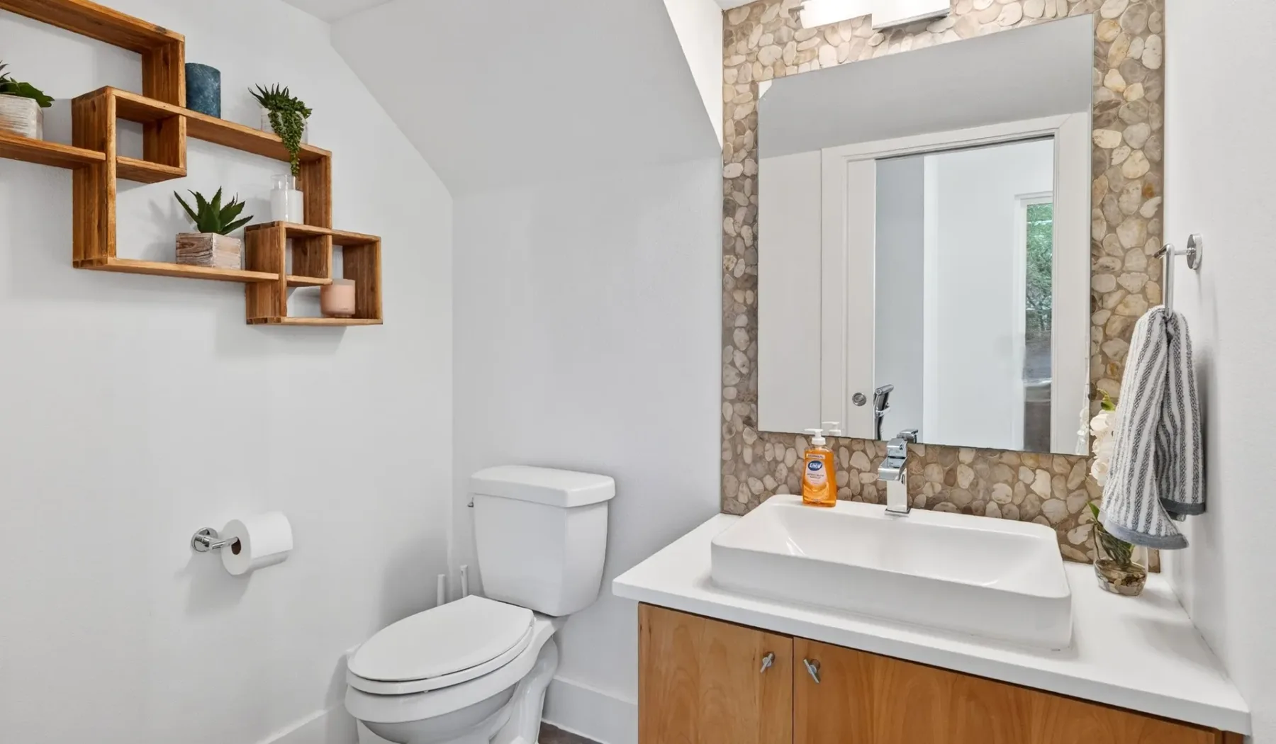 A bathroom with a sink, toilet, and stone-patterned wall around the mirror.