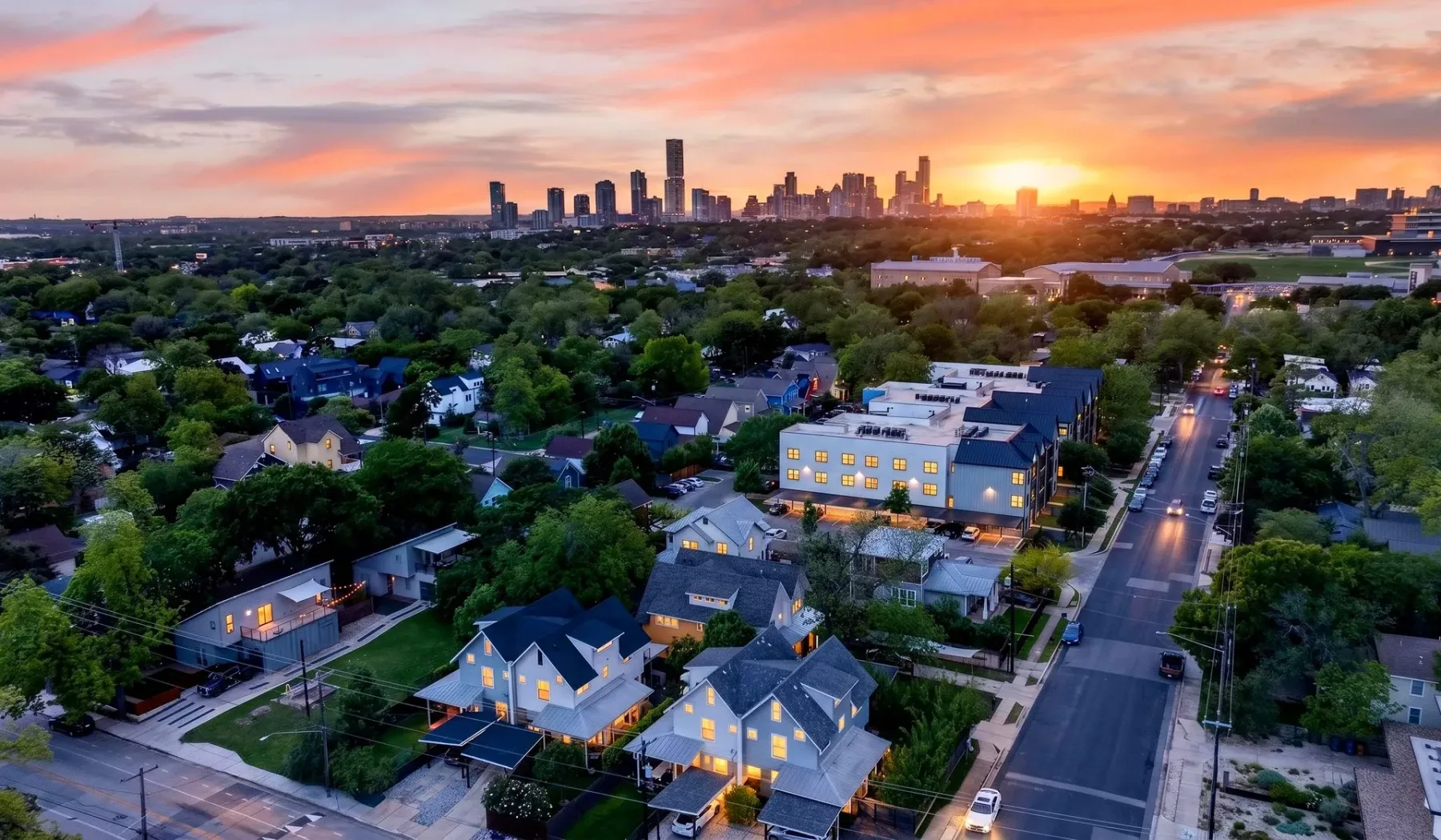Vista aérea de un barrio arbolado y el horizonte de la ciudad al atardecer.