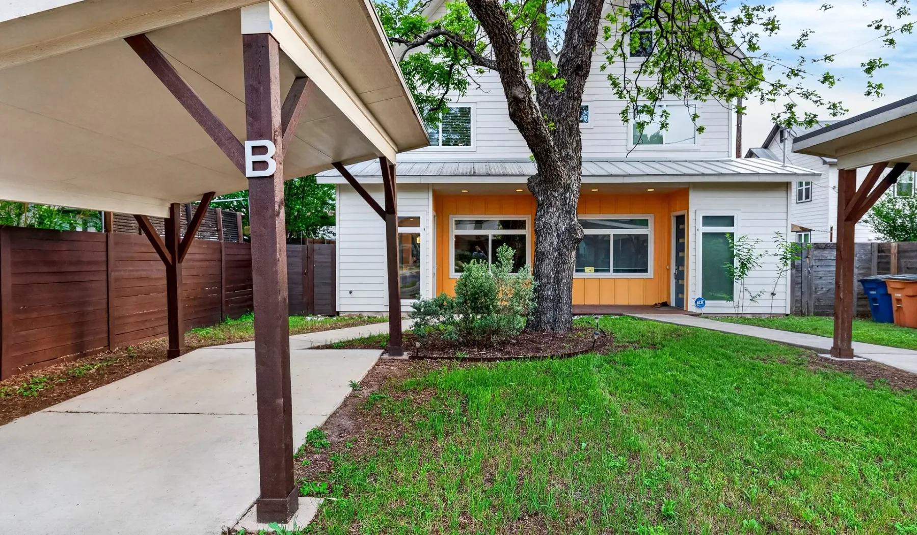 A grassy backyard with a large tree and covered patio structures.