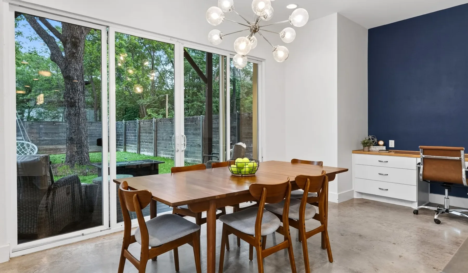 A dining area with a wooden table beside large glass doors overlooking greenery.