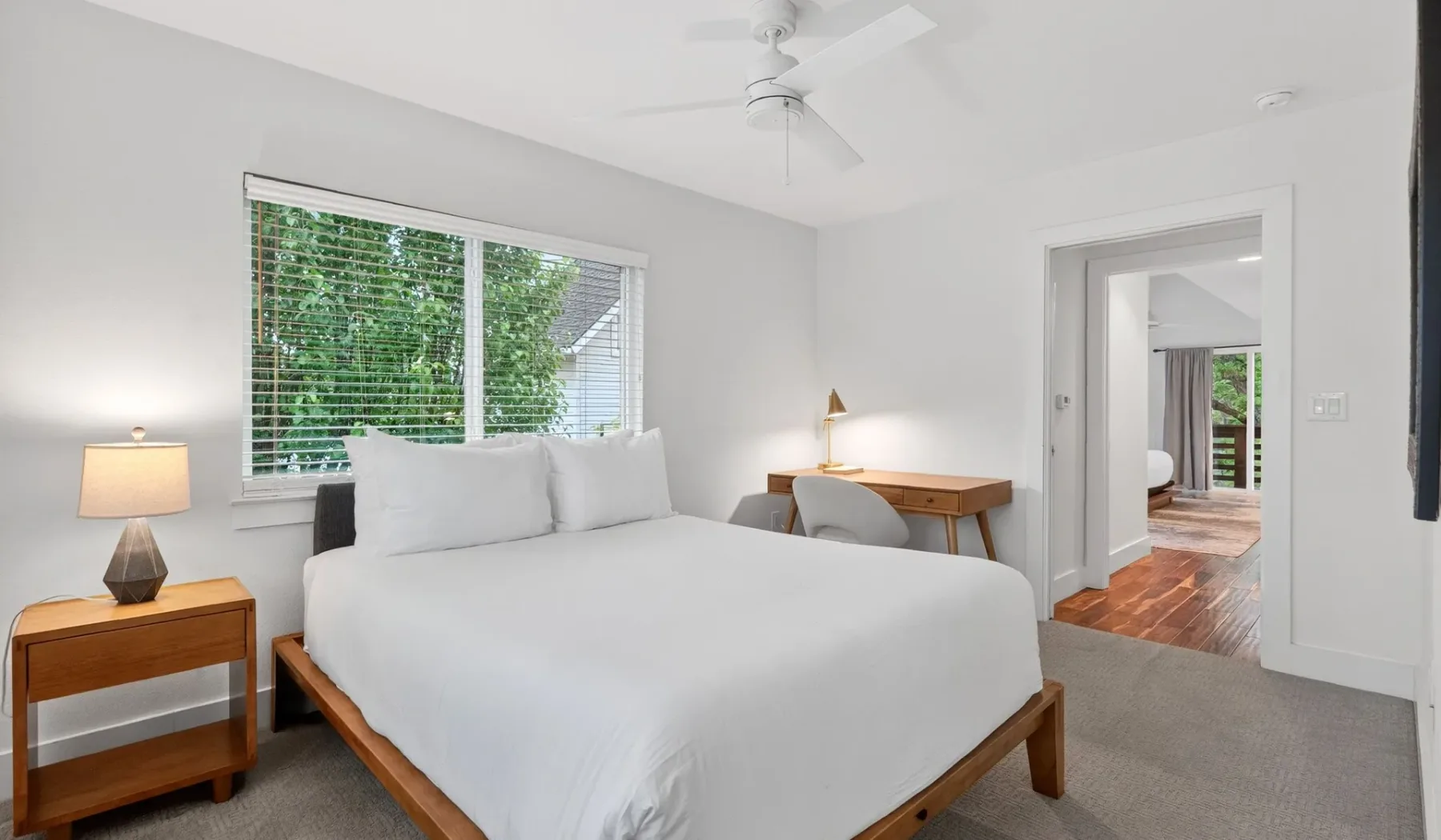 A bright bedroom with a white bed and a desk beside the window.