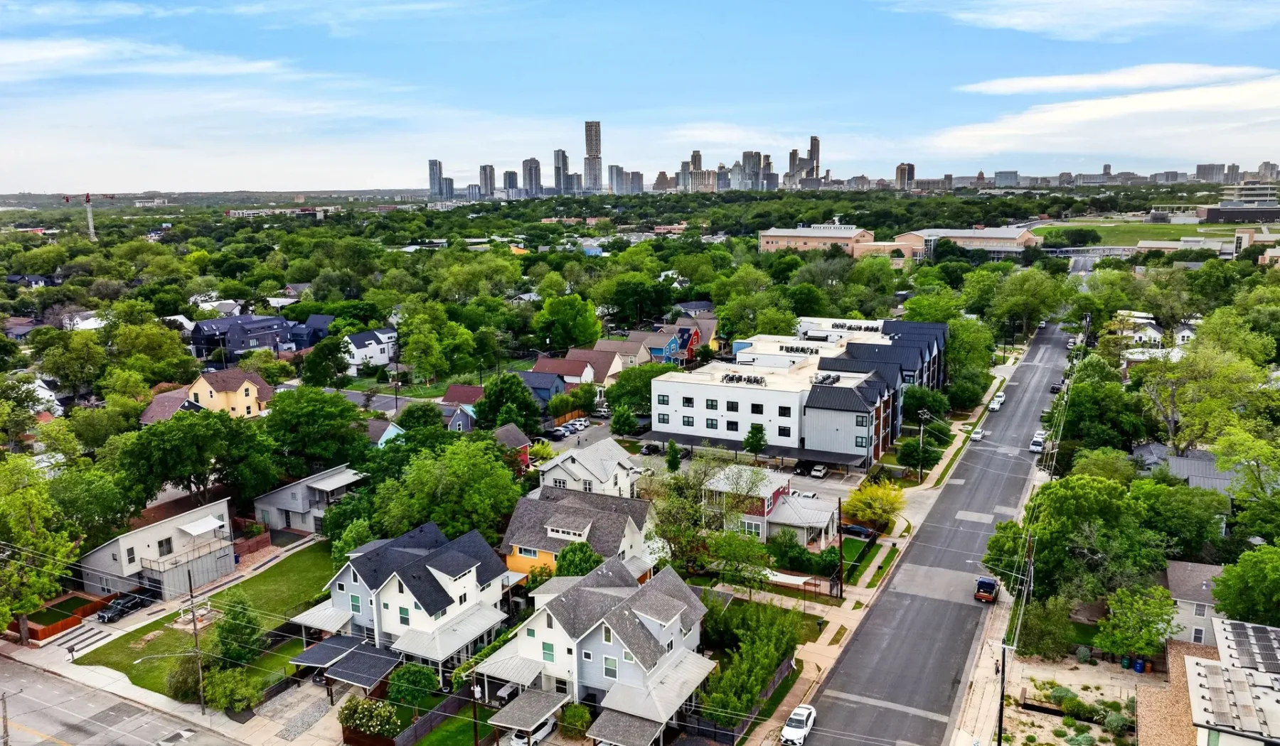Aerial view of a leafy residential neighborhood with a city skyline in the distance.