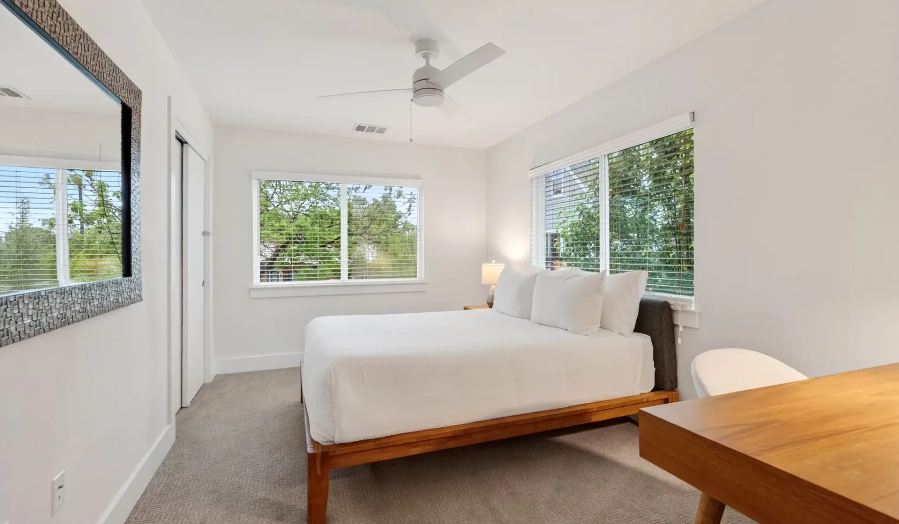 A bright bedroom with a bed beneath windows overlooking greenery.