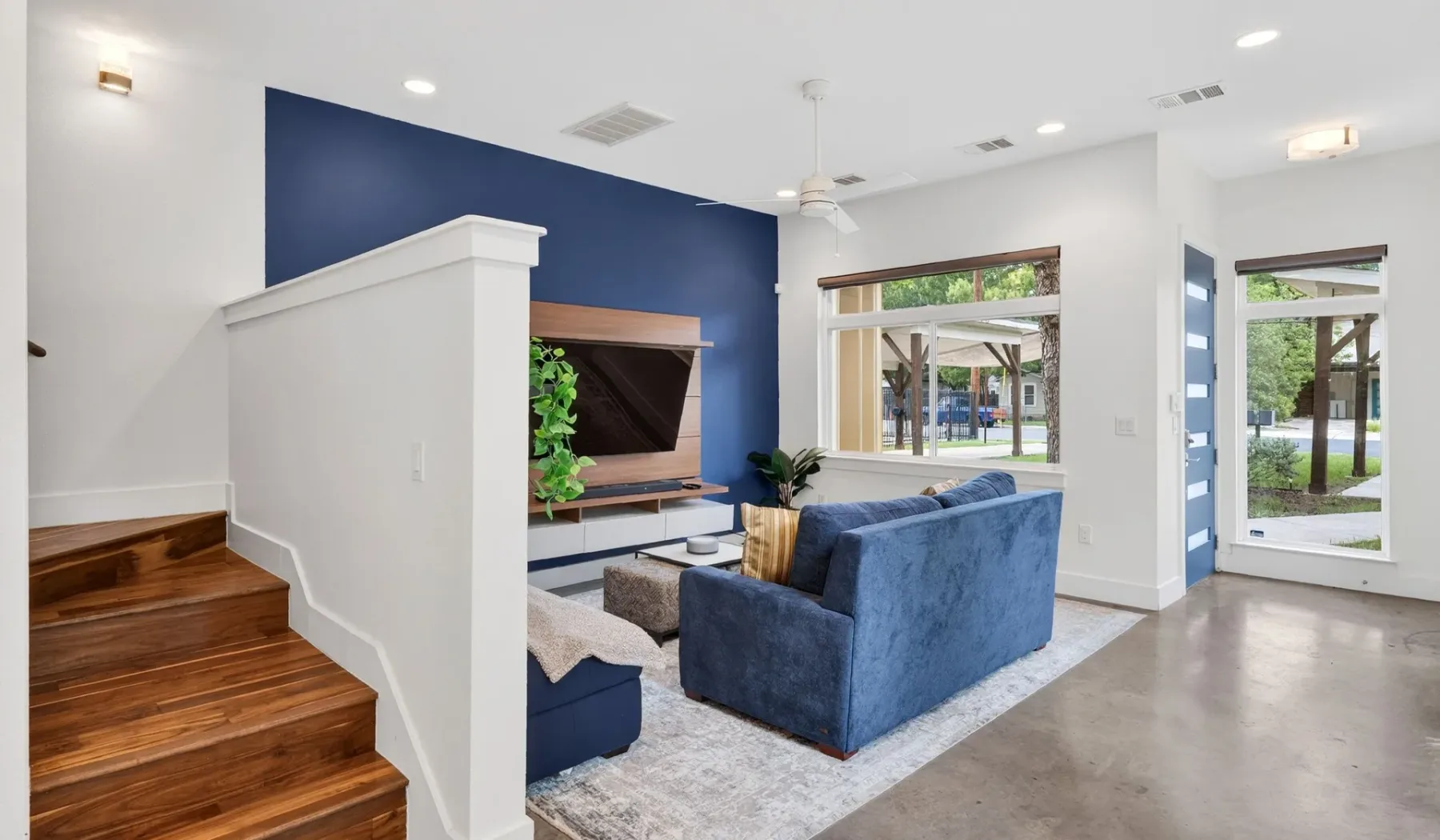 A living room with blue seating, a television, and large windows.