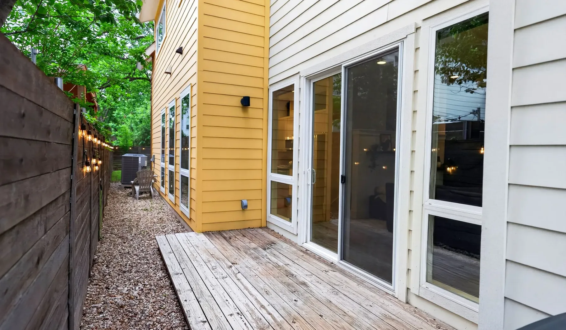 A narrow outdoor passage beside a house opens onto a wooden deck.