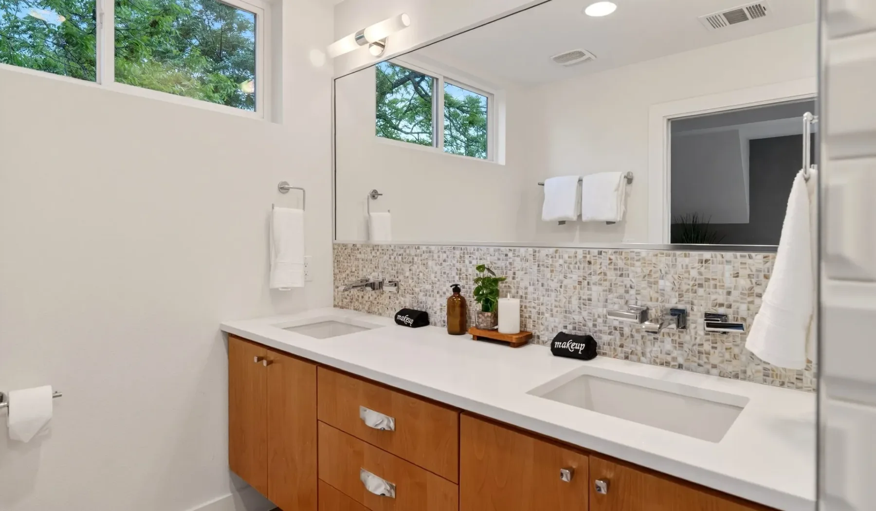 A bright bathroom vanity with two sinks and a tiled backsplash.