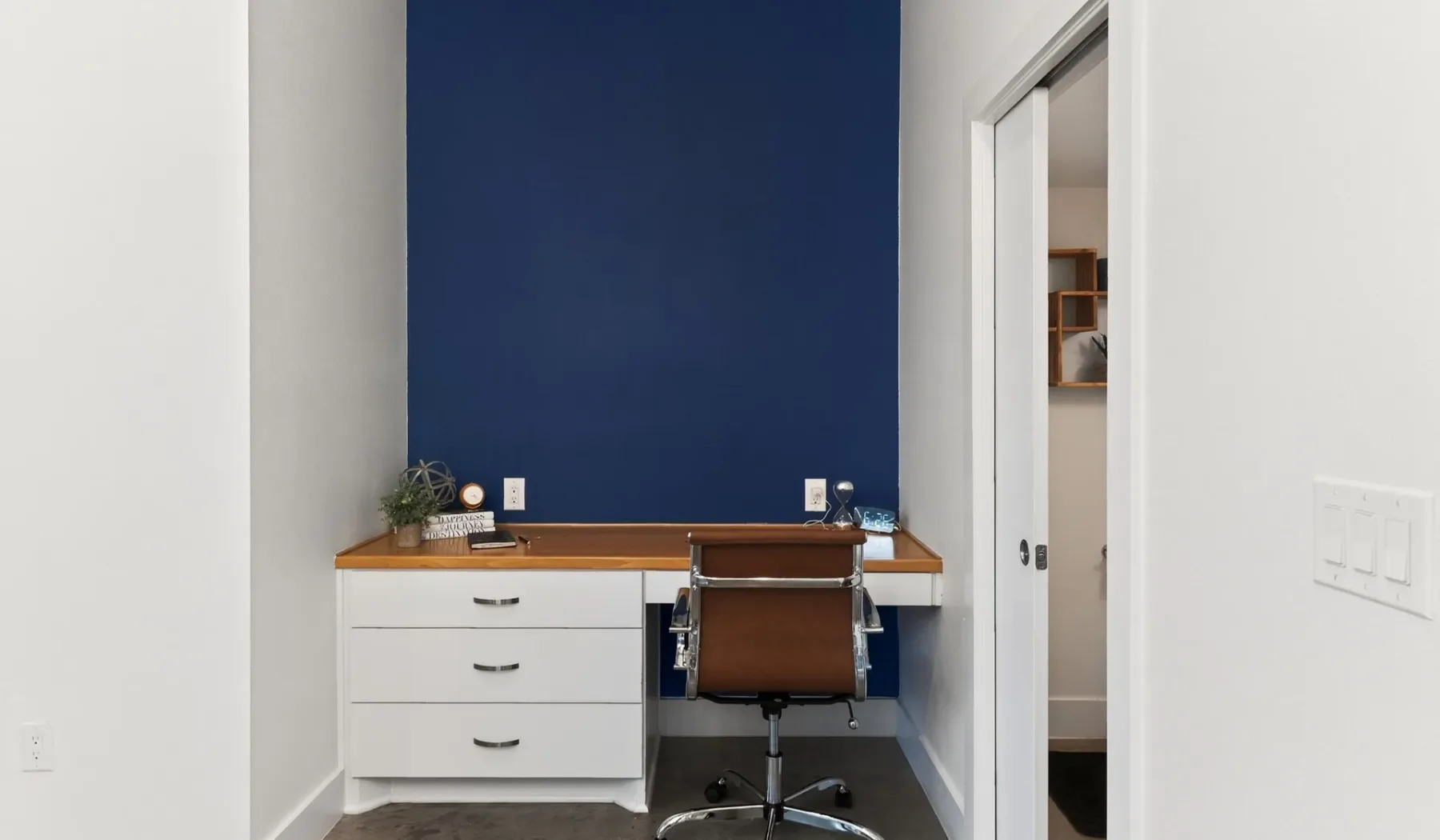 A compact desk nook with a brown chair against a blue wall.