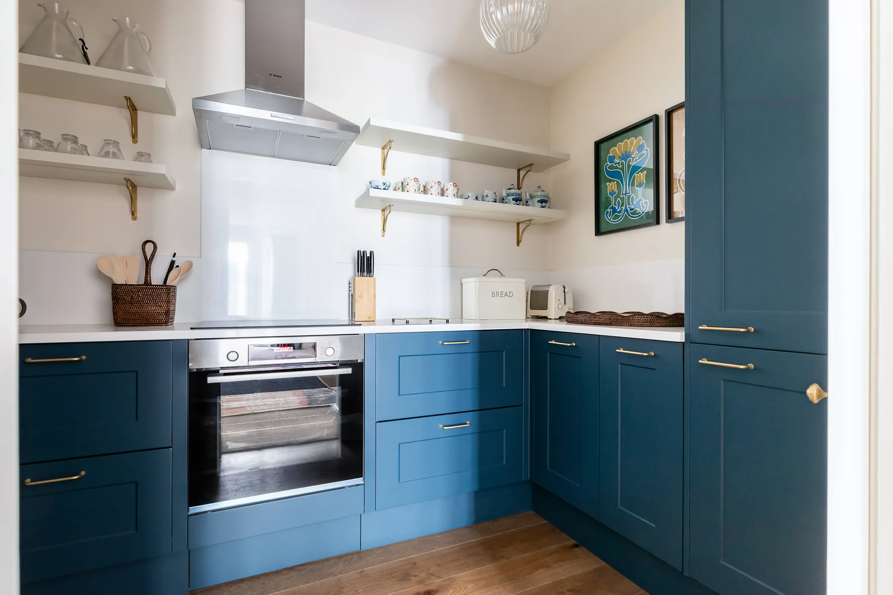 A blue-cabinet kitchen with a range, oven, and open wall shelves.