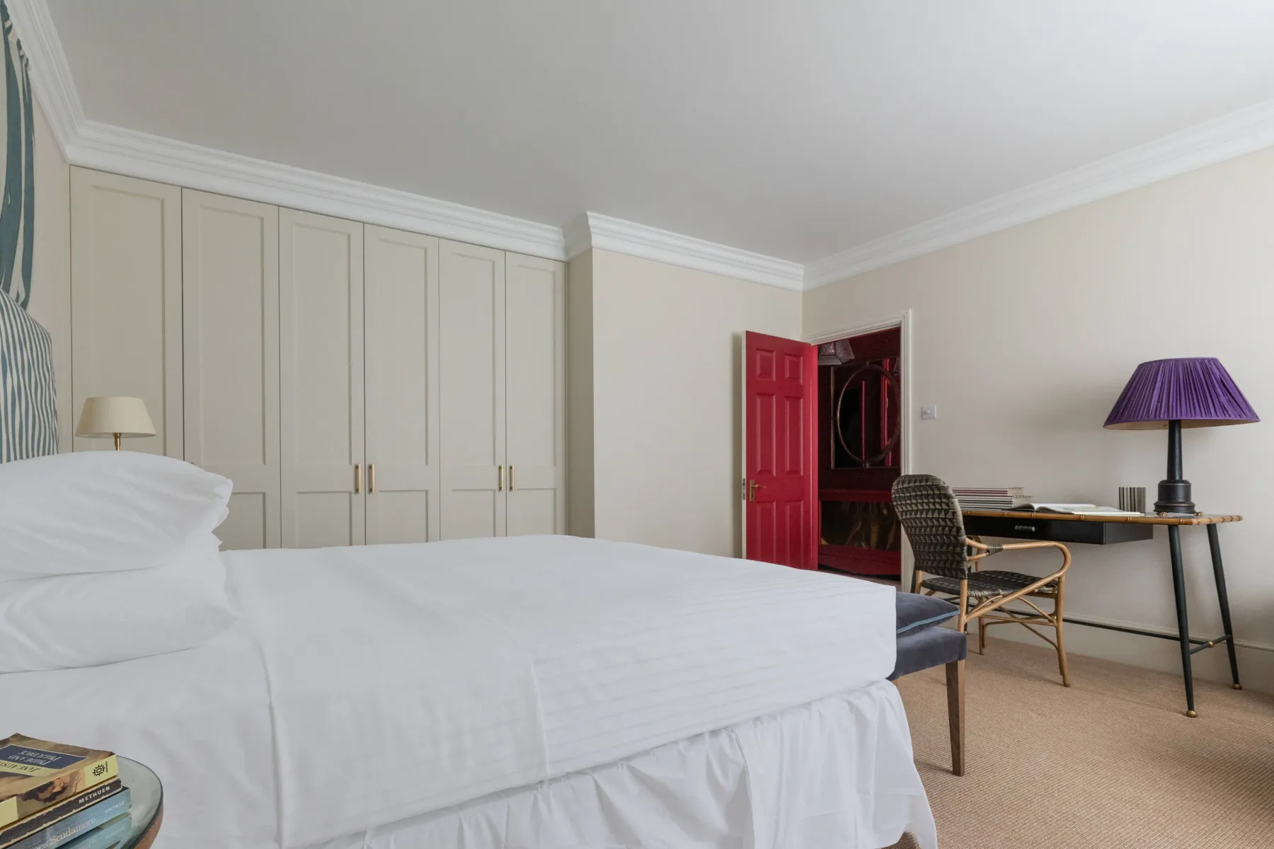 A bedroom with a bed, built-in wardrobes, and a desk beside an open red door.