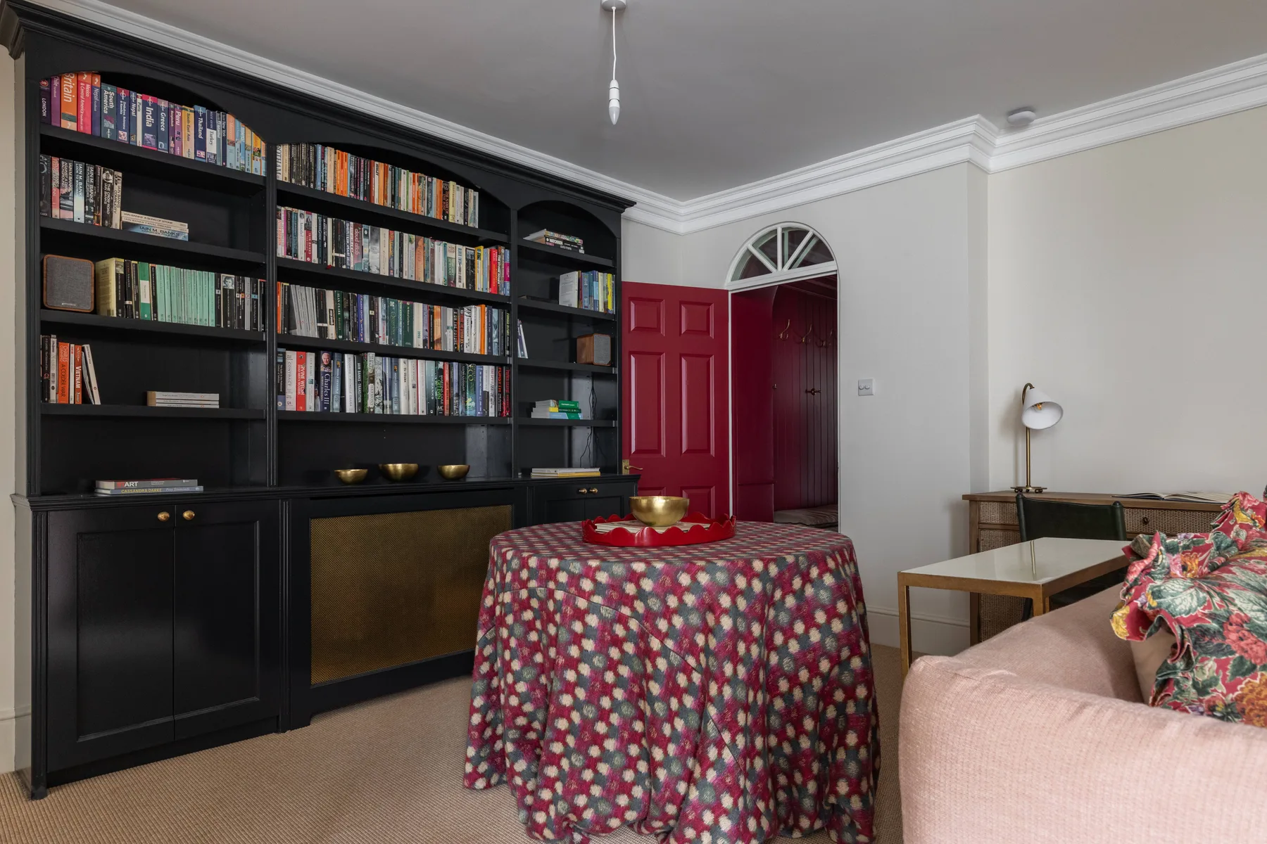 A living room with a large bookcase and a round table covered in a patterned cloth.