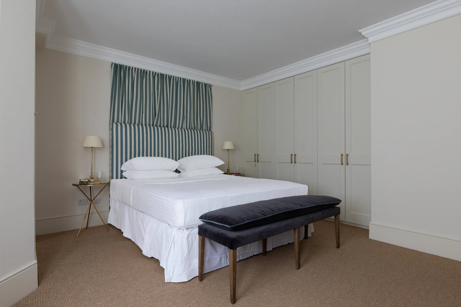 A bedroom with a neatly made bed, striped headboard, and bench at the foot.