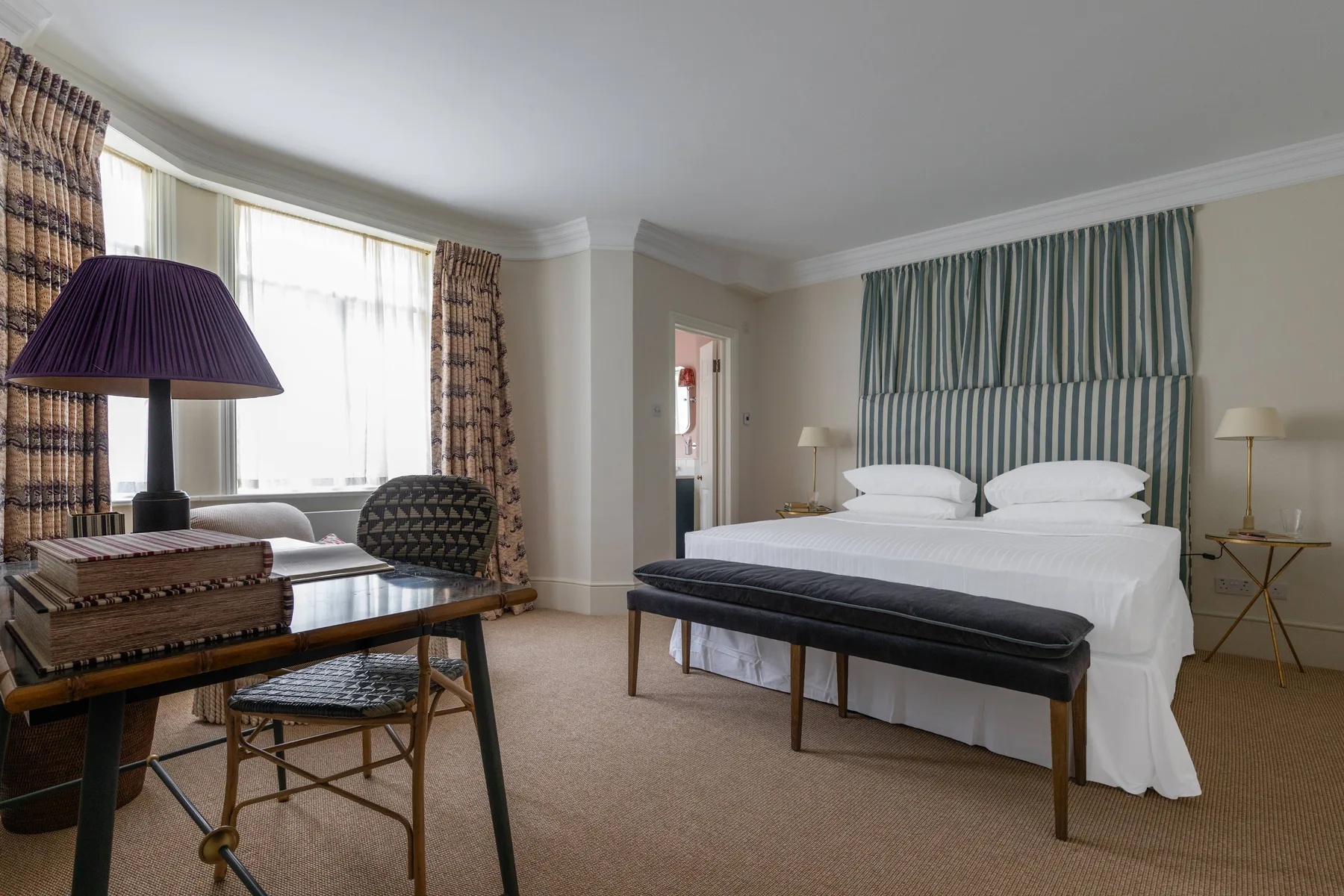 A bedroom with a bed, a bench, and a seating area beside the window.