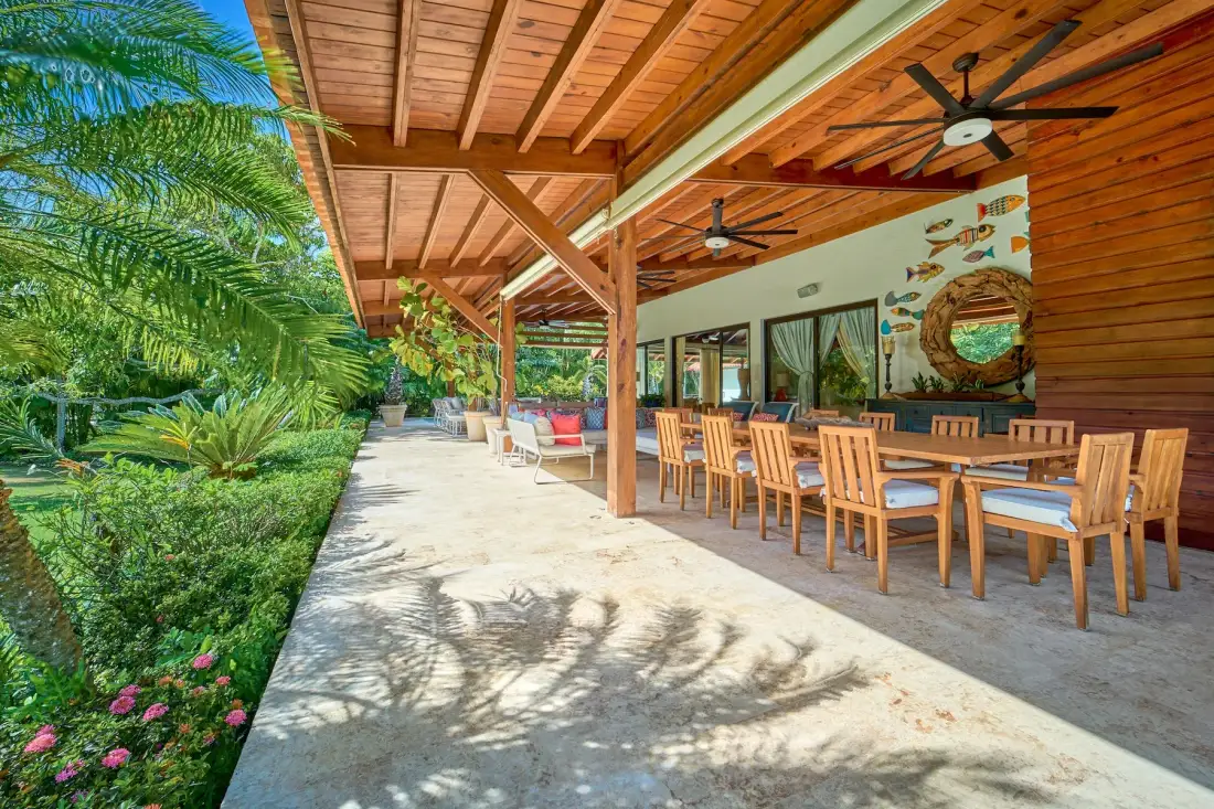 Un comedor exterior cubierto con mesas de madera junto a un jardín frondoso.