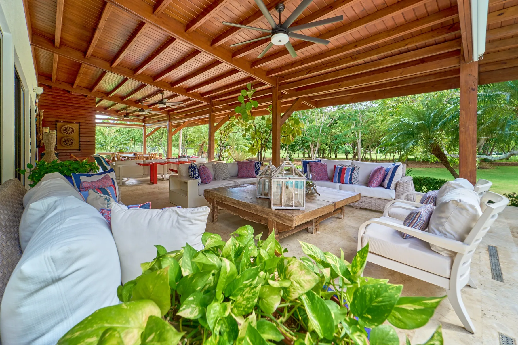 Una zona de estar exterior cubierta con asientos acolchados y una mesa de madera.