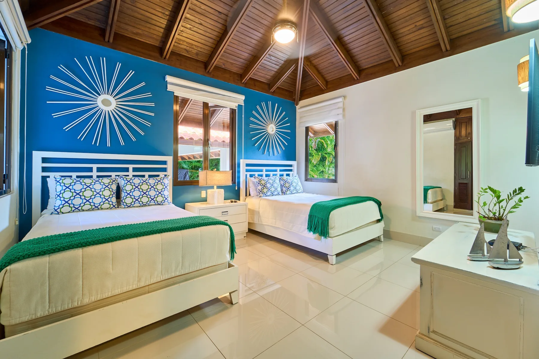Un dormitorio con dos camas, paredes azules y un techo alto de madera.