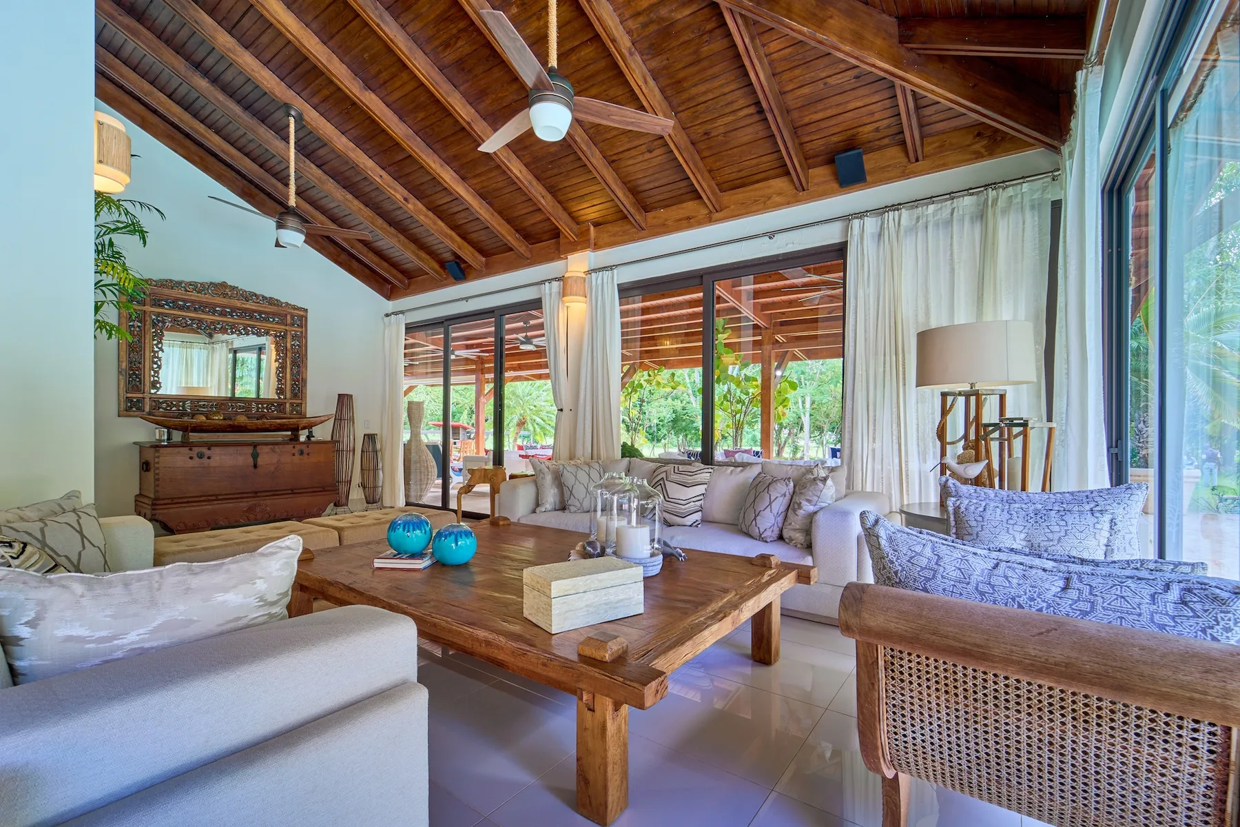 Una sala de estar luminosa con vigas de madera, grandes ventanas y asientos alrededor de una mesa de centro.
