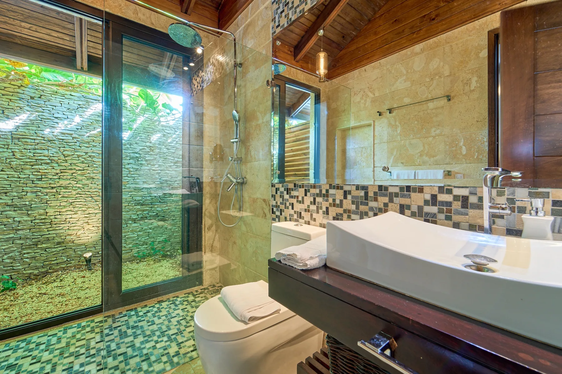 Un baño de azulejos con ducha de vidrio, inodoro y lavabo amplio.