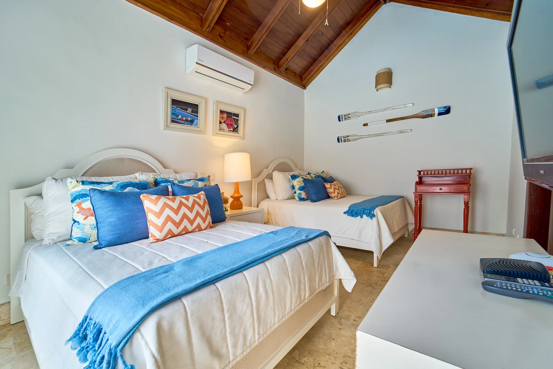 Un dormitorio luminoso con dos camas, ropa de cama azul y techo de madera.