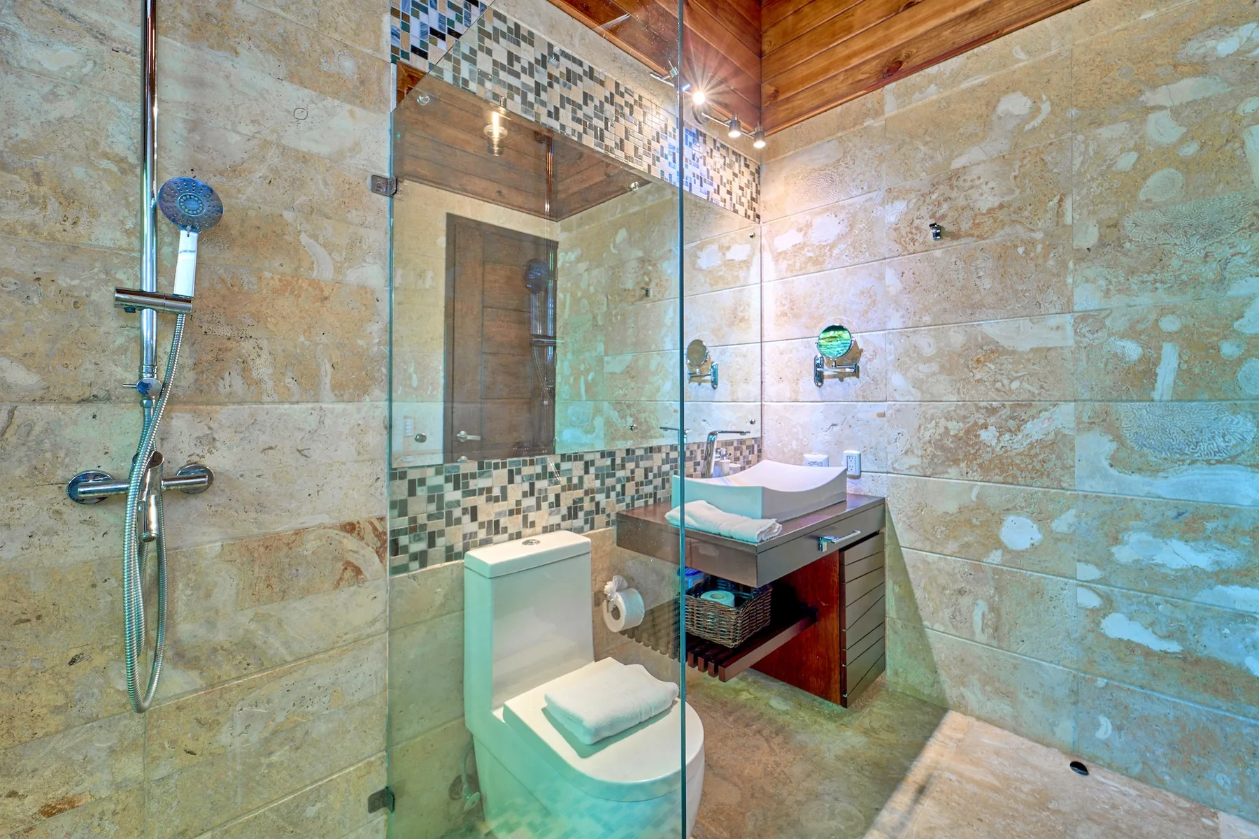 Un baño revestido de azulejos con ducha de vidrio, inodoro y lavabo.