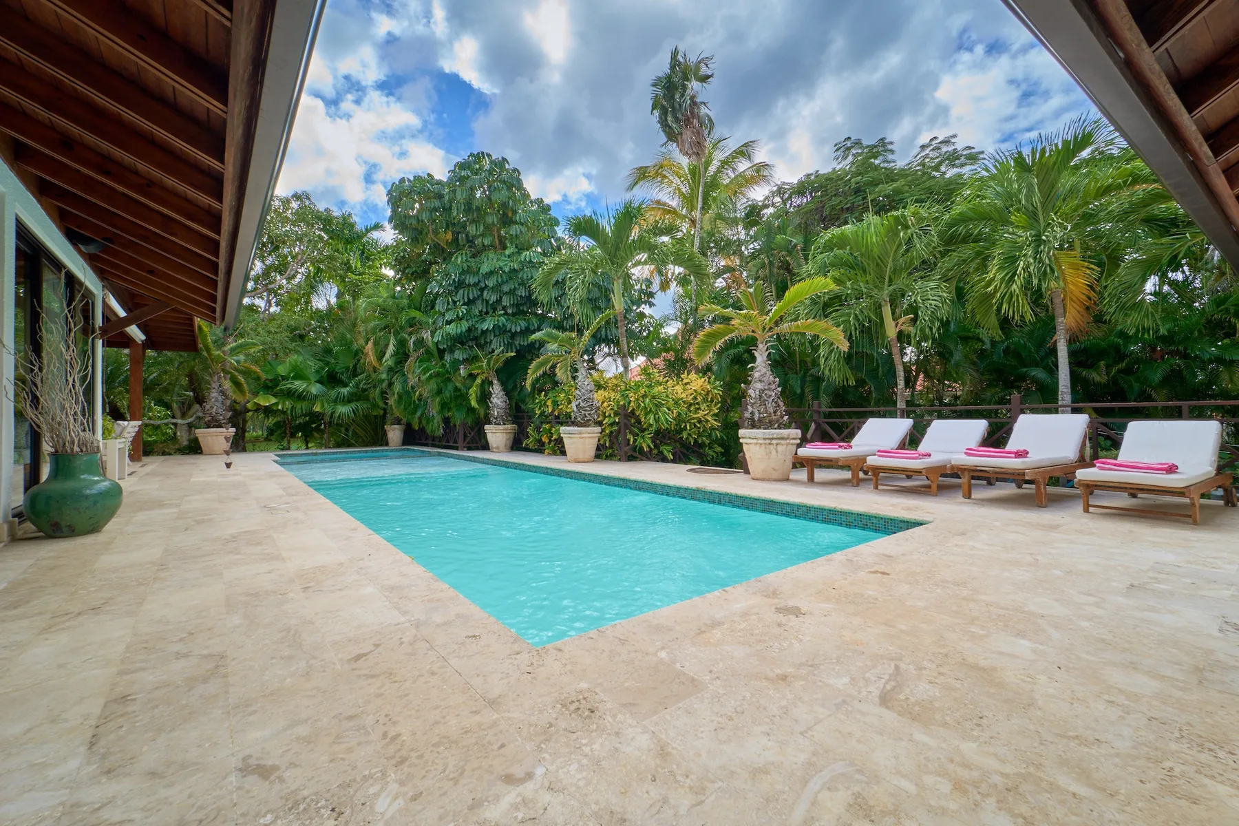 Una piscina rodeada por una terraza pavimentada, asientos y vegetación tropical.