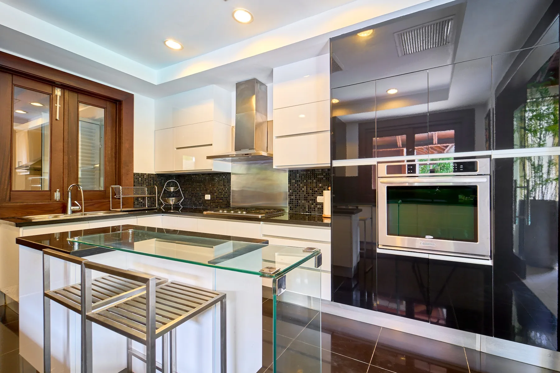 Una cocina moderna con gabinetes blancos, encimeras oscuras y una isla con superficie de vidrio.