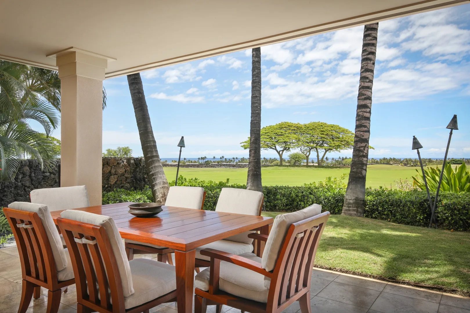A covered outdoor dining area overlooks a green lawn and distant ocean.