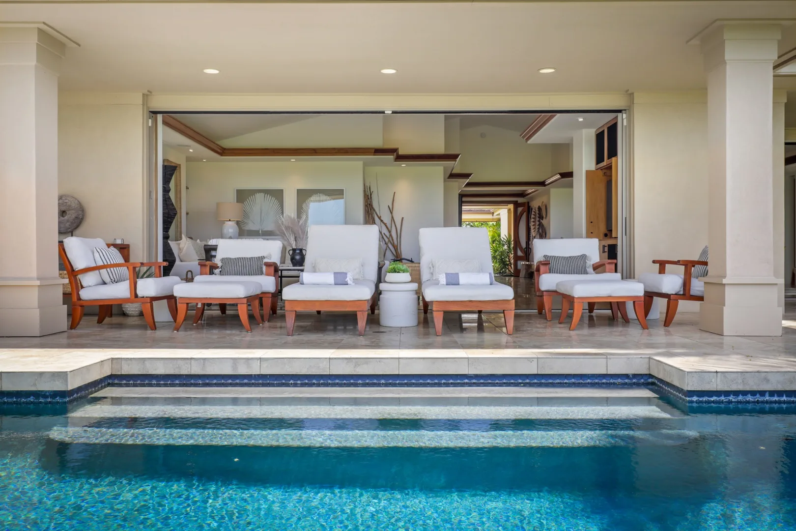 A covered patio with lounge seating opens onto a swimming pool.