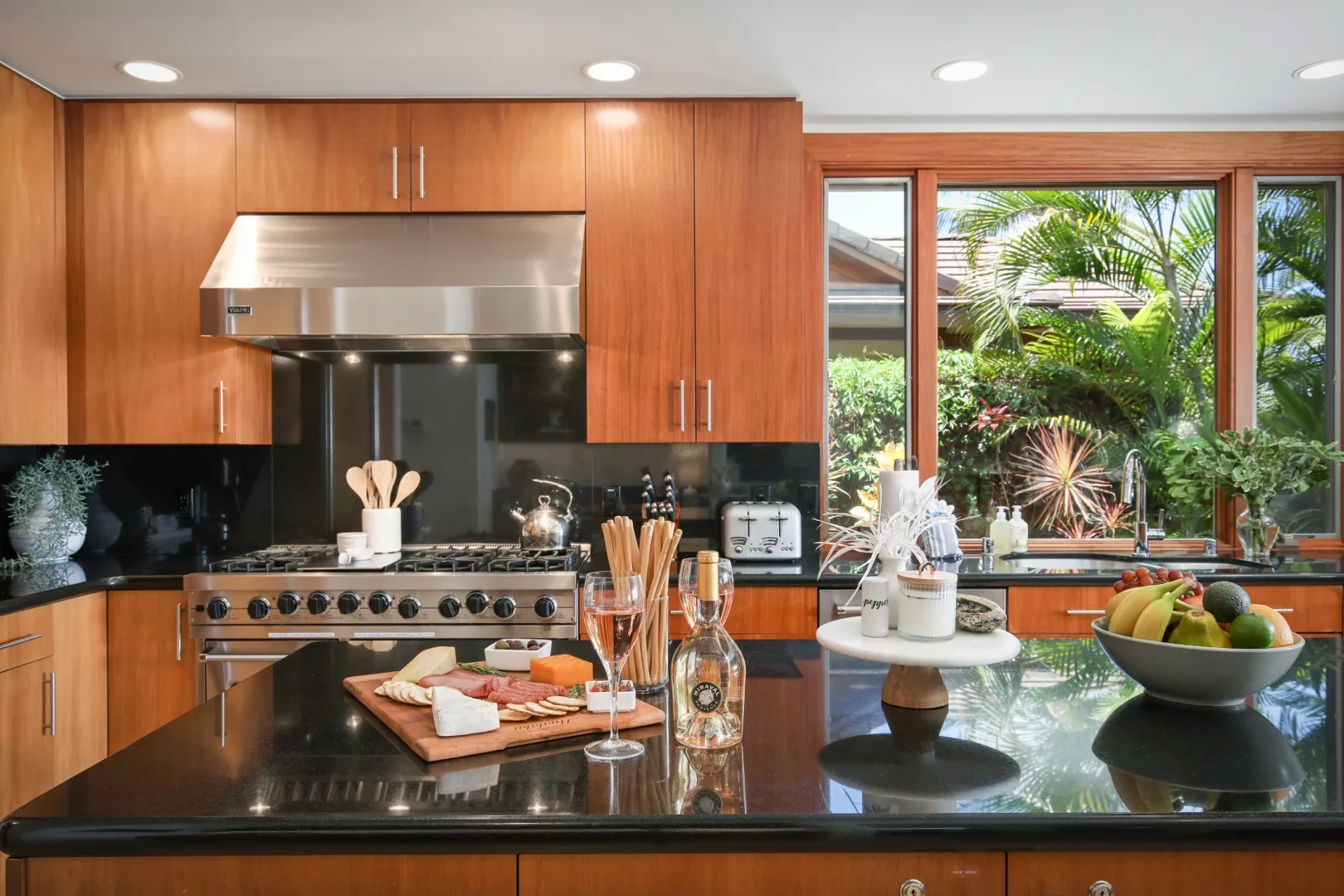 A modern kitchen with warm wood cabinetry, stainless steel appliances, and a dark island.