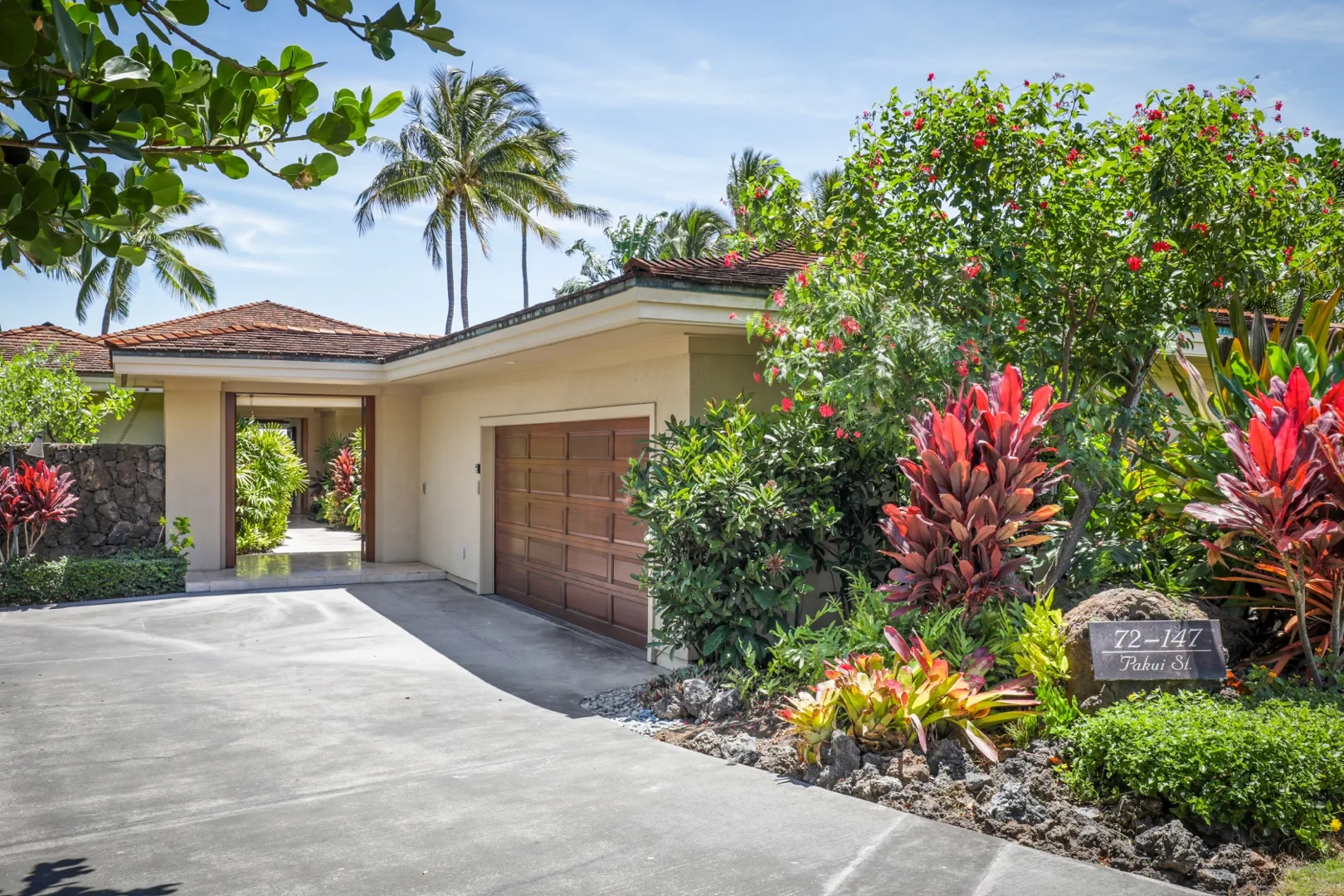 A driveway leads to a garage beside a landscaped tropical garden.