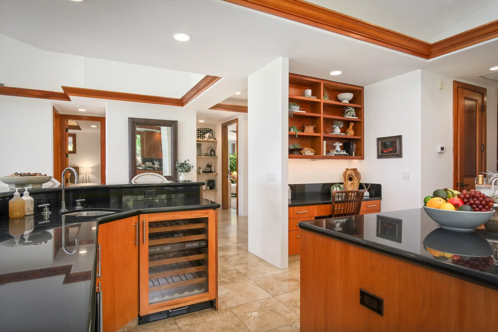 A kitchen with wood cabinetry, dark countertops, and a central wine cooler.