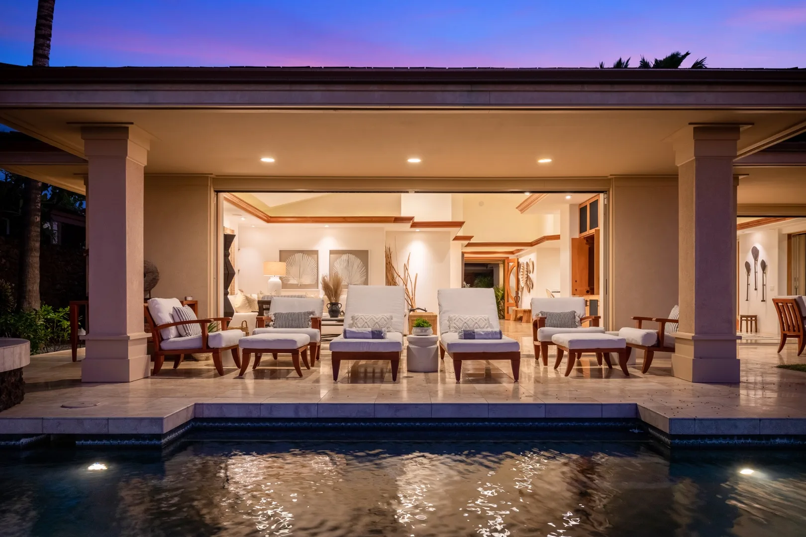 An illuminated outdoor seating area opens onto a pool at dusk.