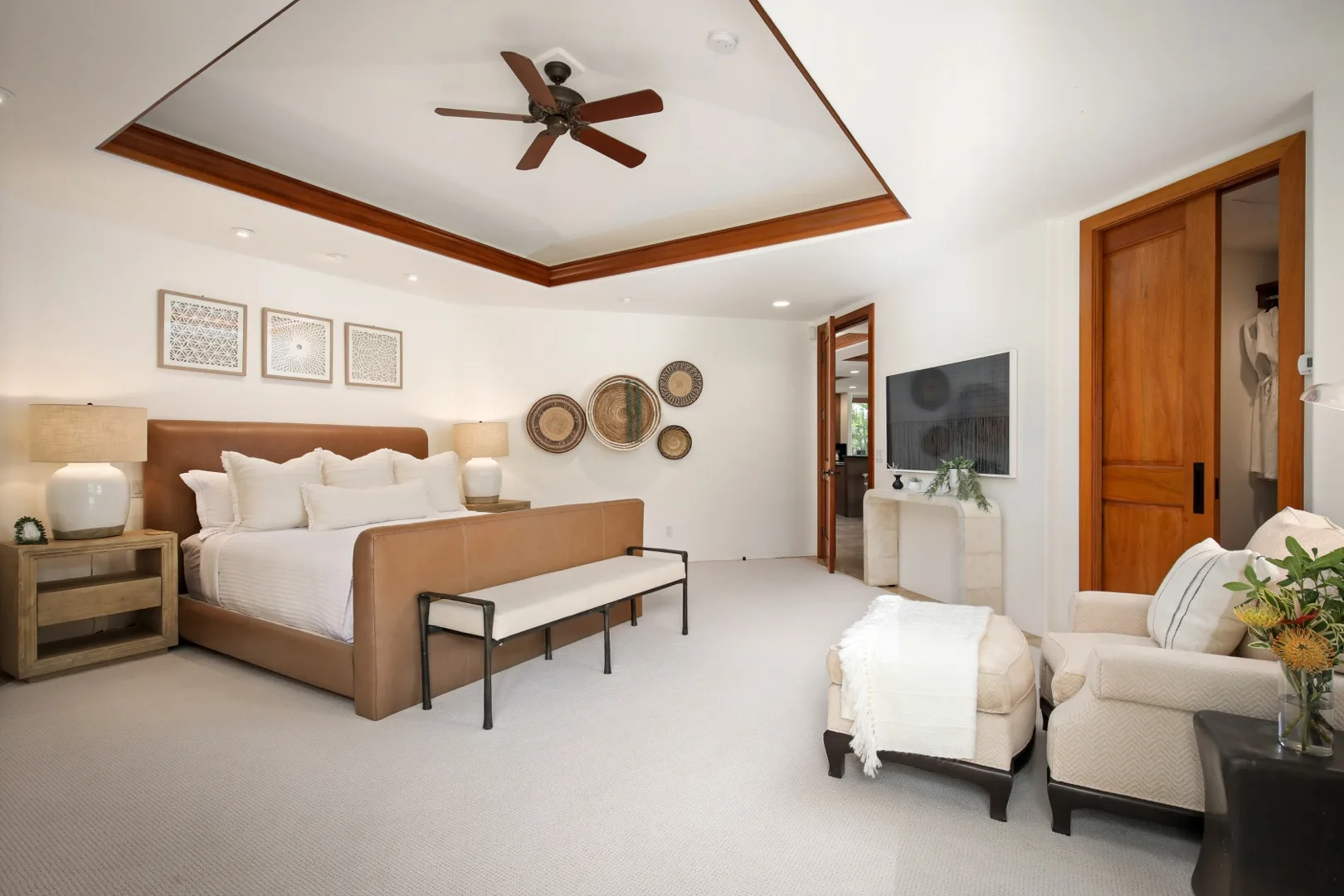 A bedroom with a large bed, a ceiling fan, and seating by the television.