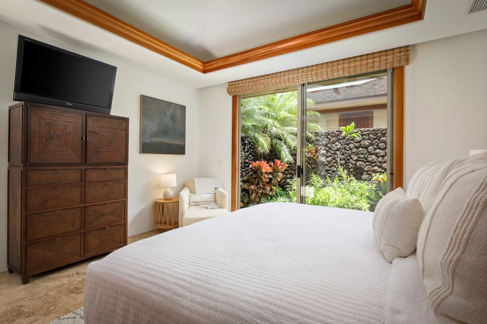 A bedroom with a large bed beside a window overlooking a garden.