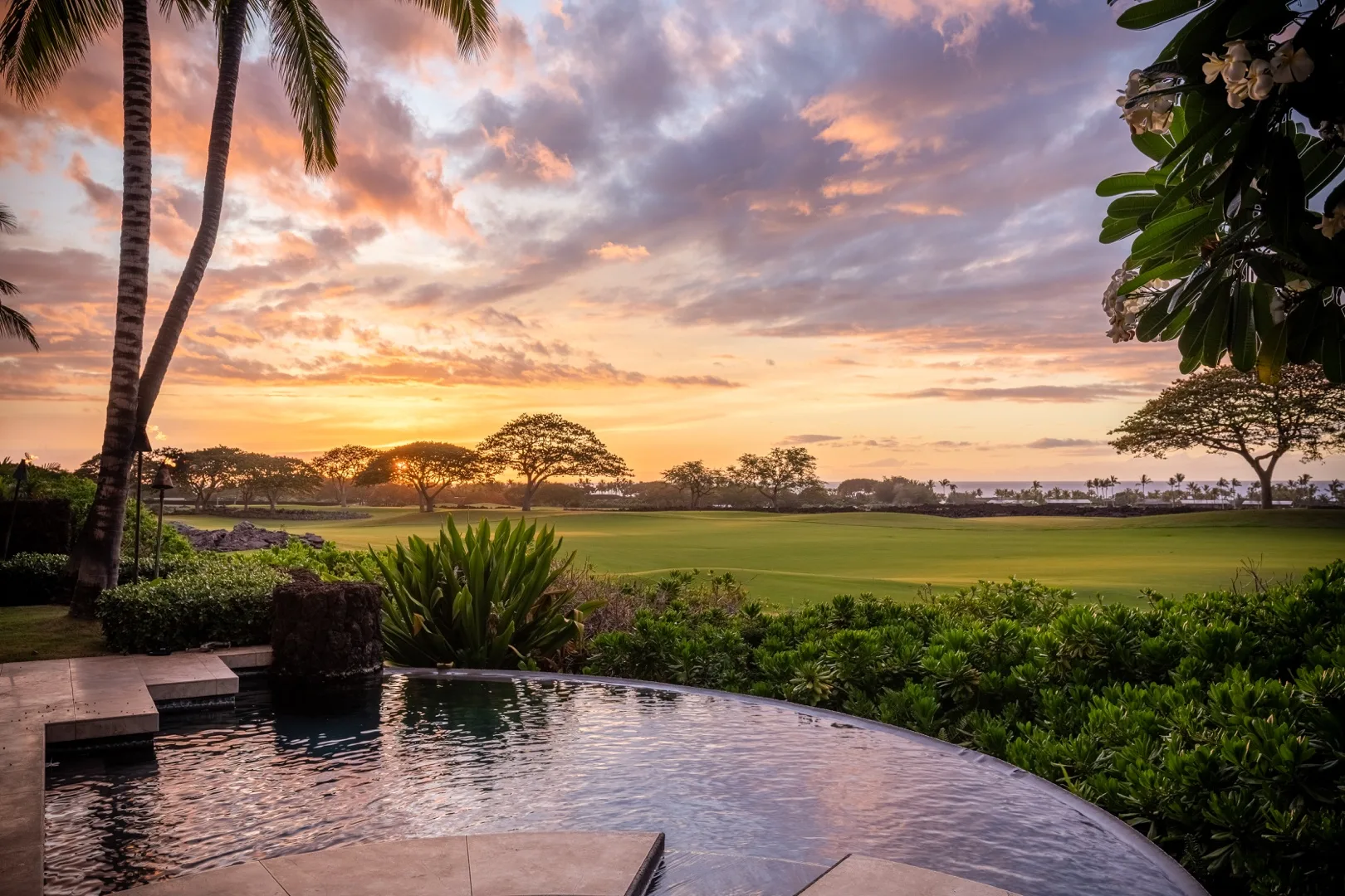 A pool overlooks a green landscape beneath a colorful sunset sky.