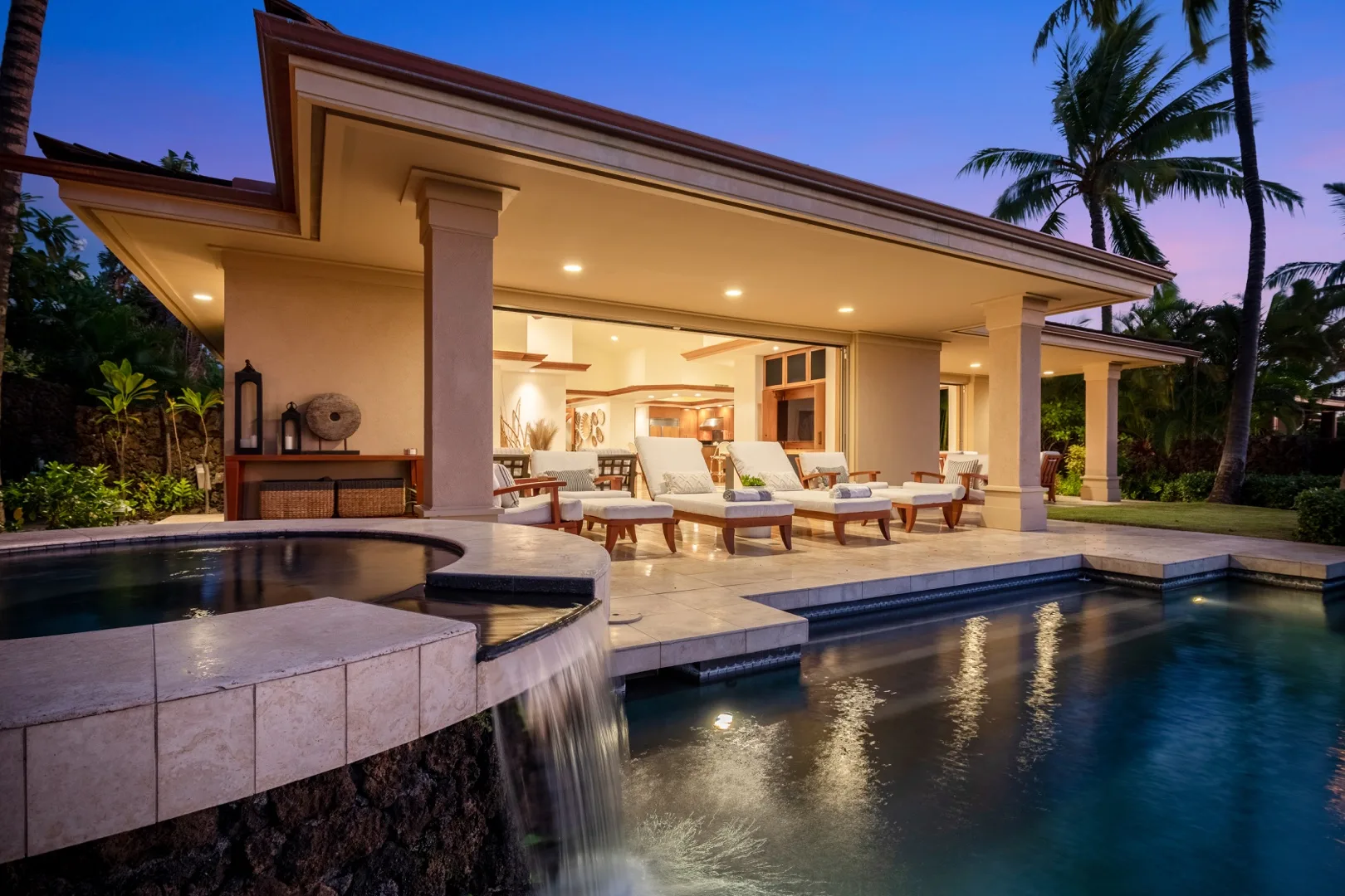 A lit open-sided pavilion overlooks a swimming pool and a small cascading water feature.