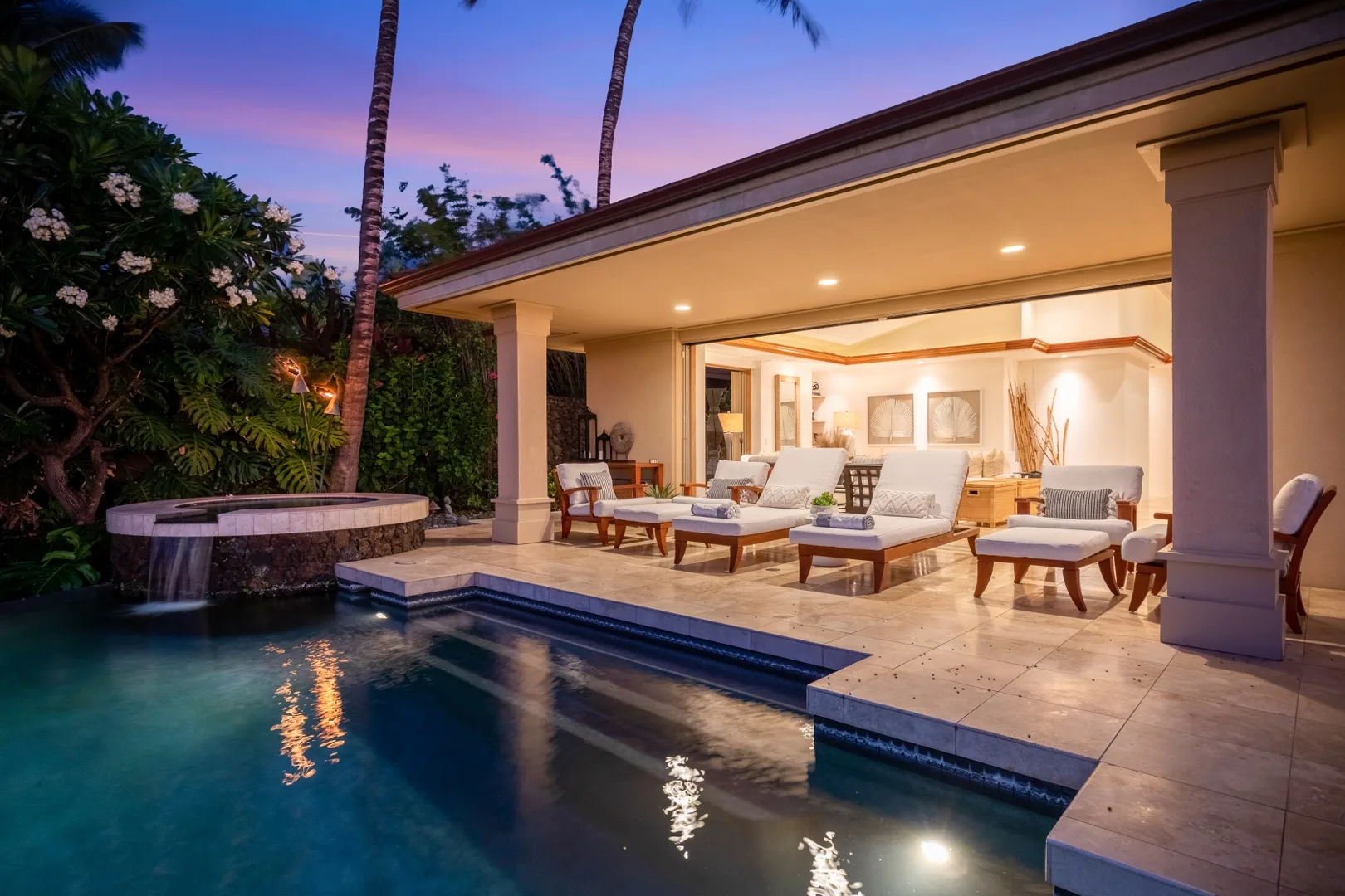 A poolside patio with outdoor seating opens onto a brightly lit interior.