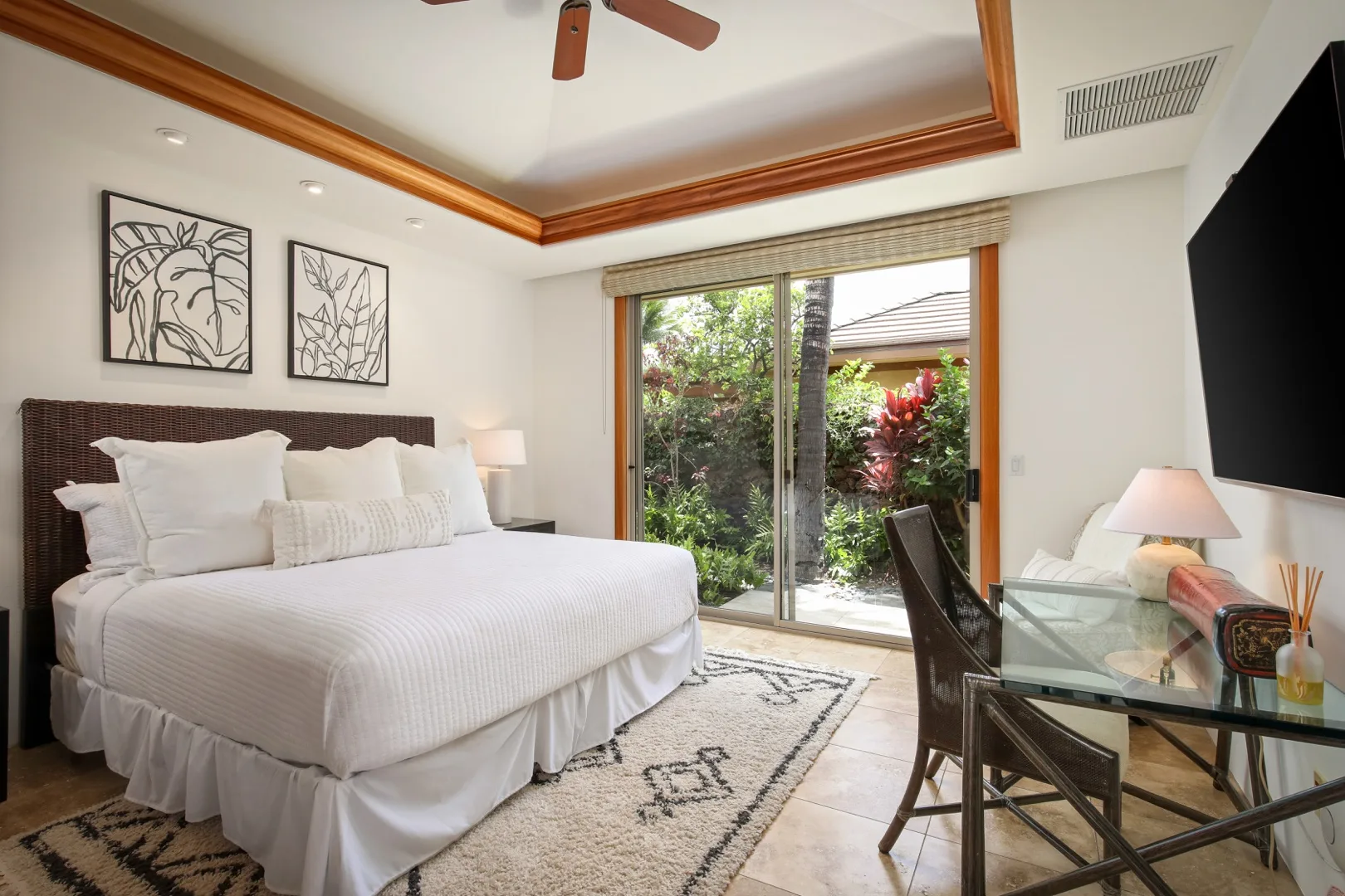 A bedroom with a large bed, framed artwork, and glass doors opening onto a garden.