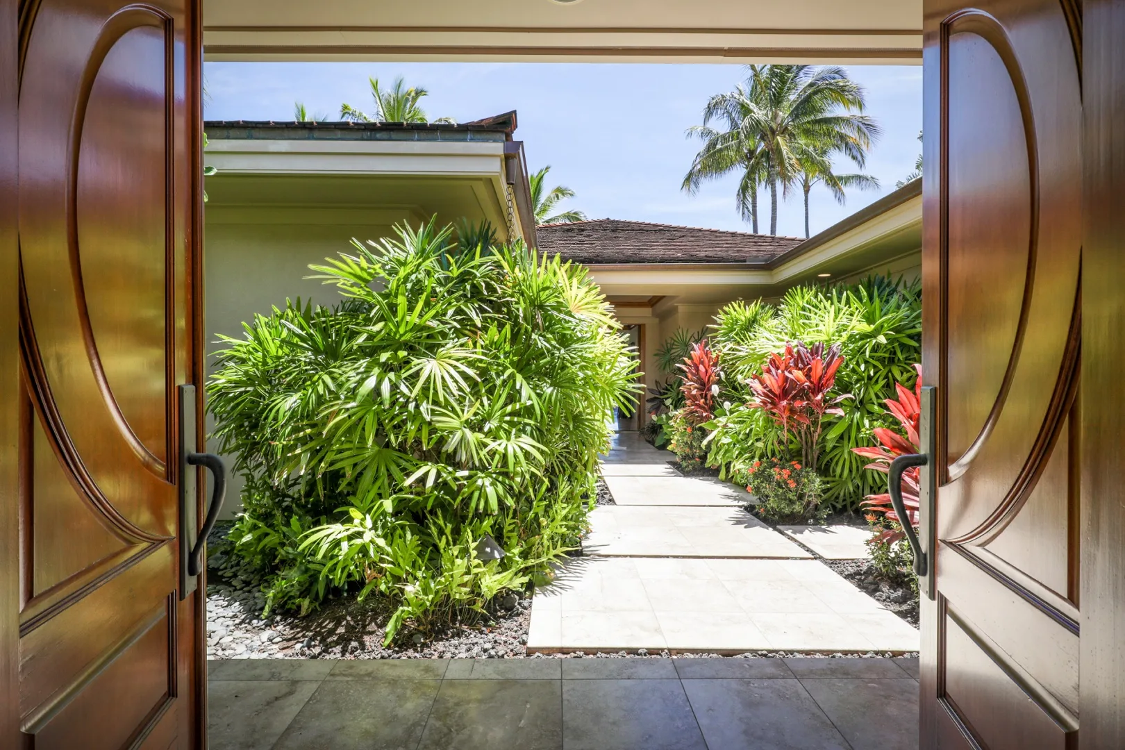 A paved garden walkway leads between lush tropical plants toward a building.