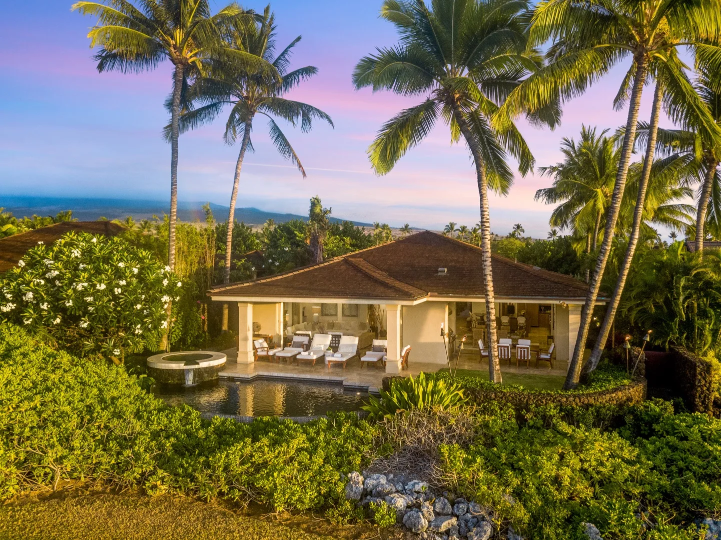 A tropical house sits among palm trees and lush greenery.