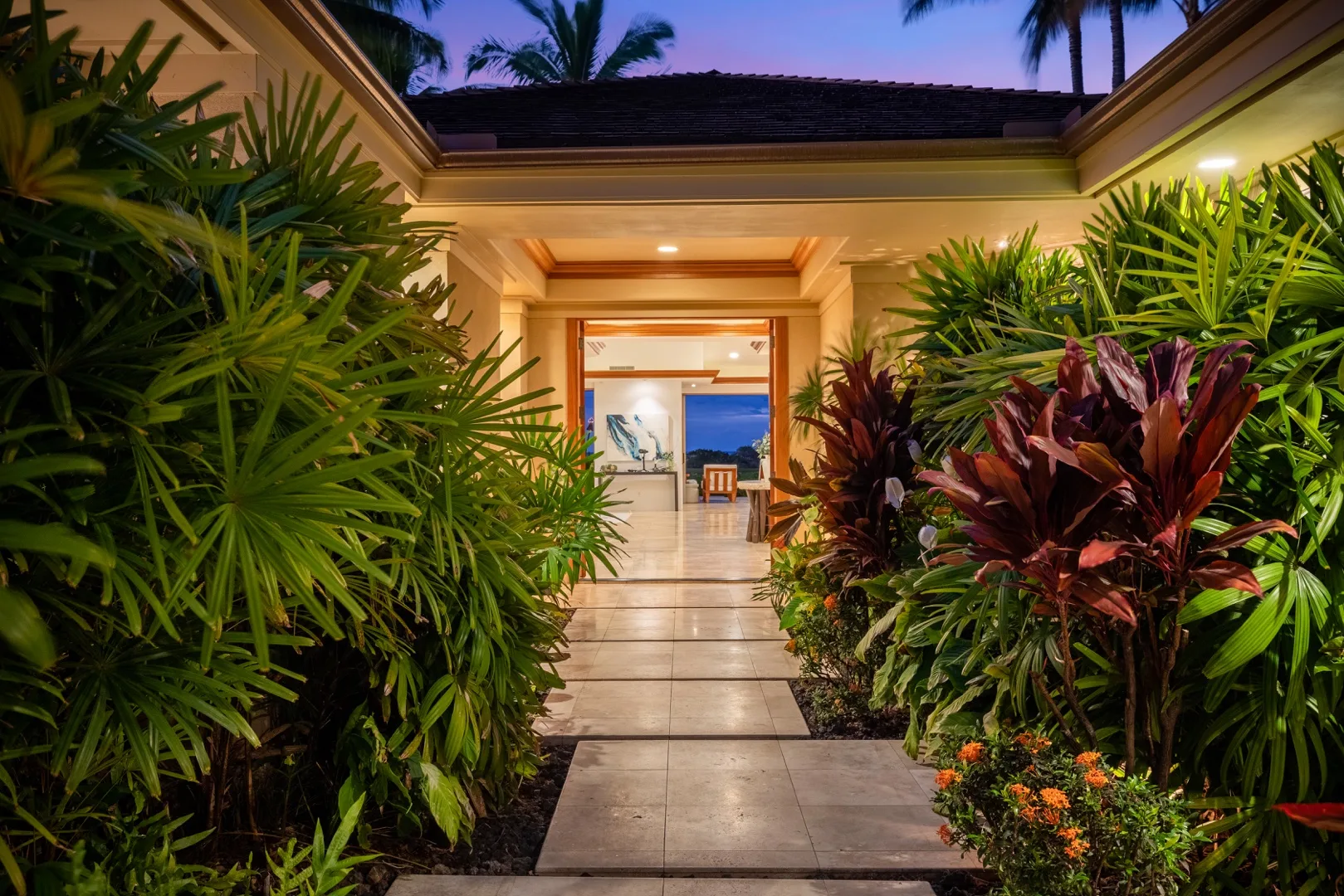 A landscaped walkway leads through tropical plants toward an open building entrance.
