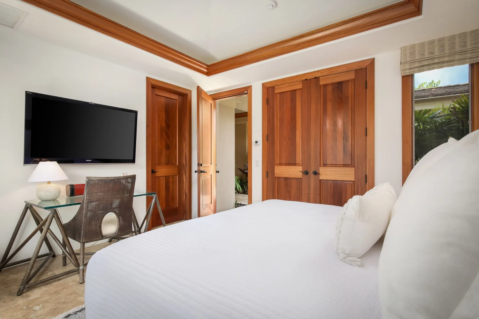 A bedroom with a bed, wall-mounted television, and wooden doors.